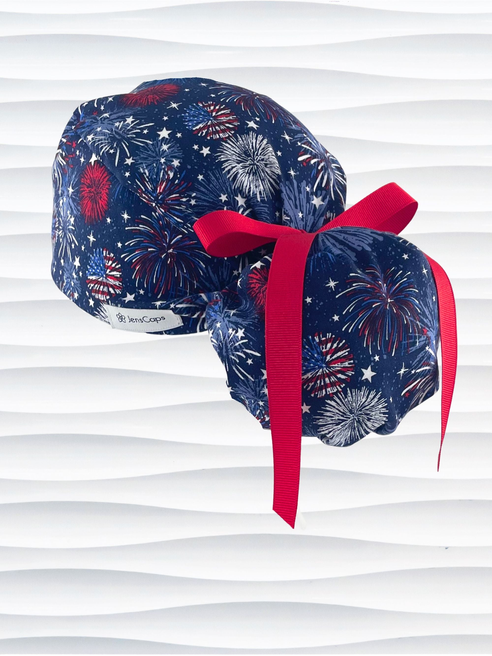 Ponytail pouch style surgical scrub cap by JensCaps with fireworks and stars in red white and blue all over navy blue cotton fabric.