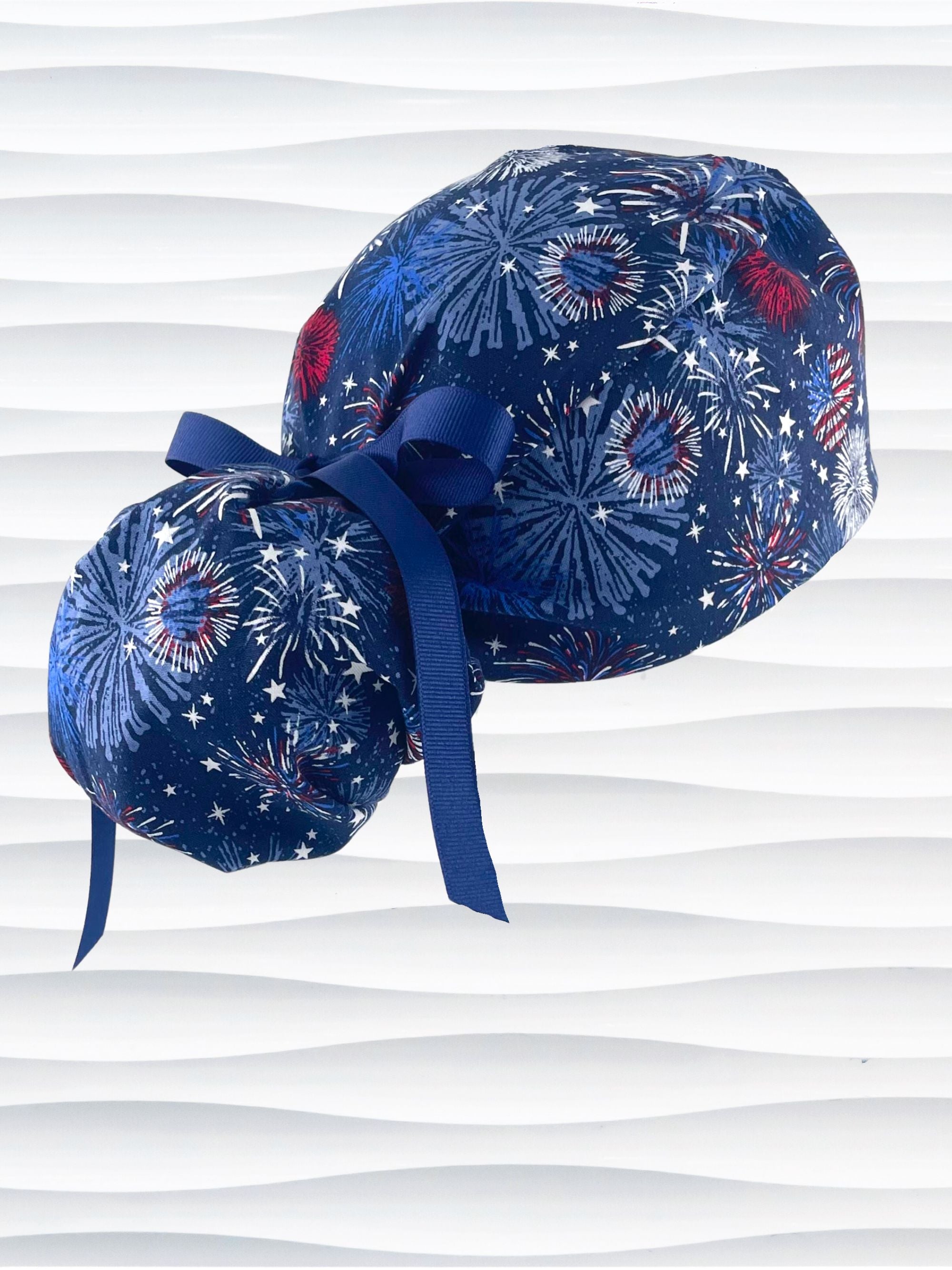 Ponytail pouch style surgical scrub cap by JensCaps with fireworks and stars in red white and blue all over navy blue cotton fabric.