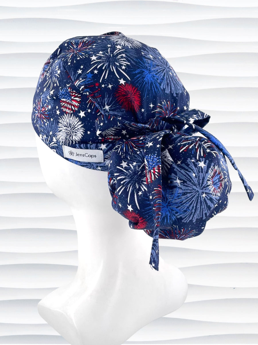 Ponytail pouch style surgical scrub cap by JensCaps with fireworks and stars in red white and blue all over navy blue cotton fabric.