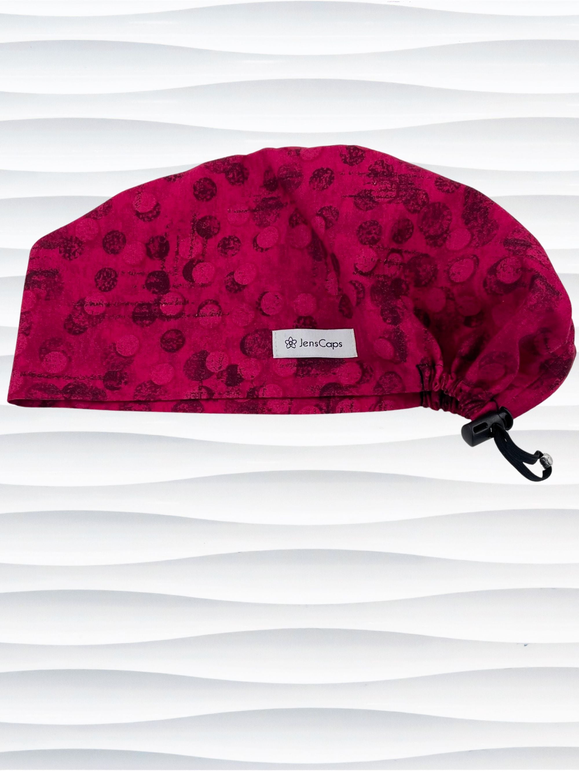 Euro Pixie style surgical scrub cap with a muted pattern of black circles and lines on deep red or magenta cotton fabric.