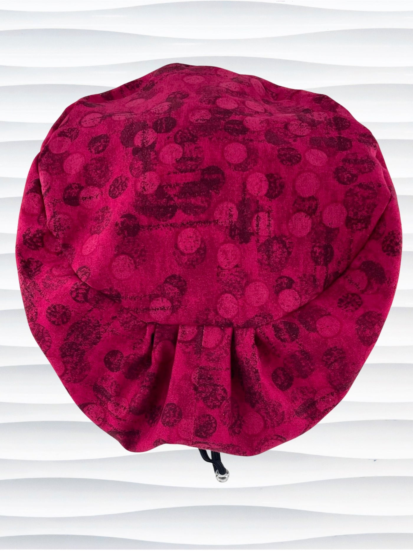 Euro Pixie style surgical scrub cap with a muted pattern of black circles and lines on deep red or magenta cotton fabric.