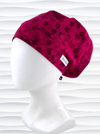 Euro Pixie style surgical scrub cap with a muted pattern of black circles and lines on deep red or magenta cotton fabric.