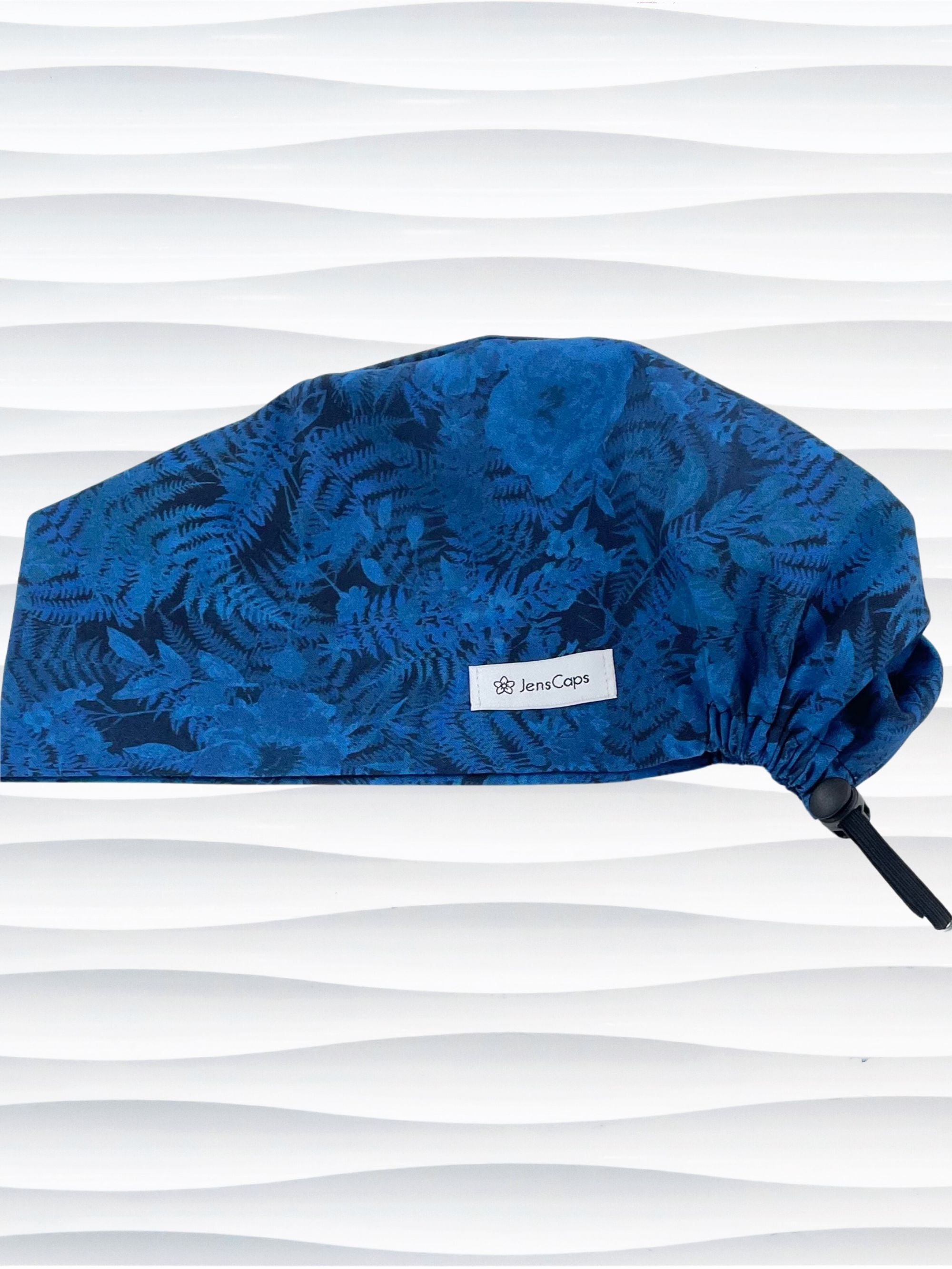 Euro Pixie style surgical scrub cap with a muted pattern of flowers, ferns, and leaves in dark blue on a deep royal blue cotton fabric.