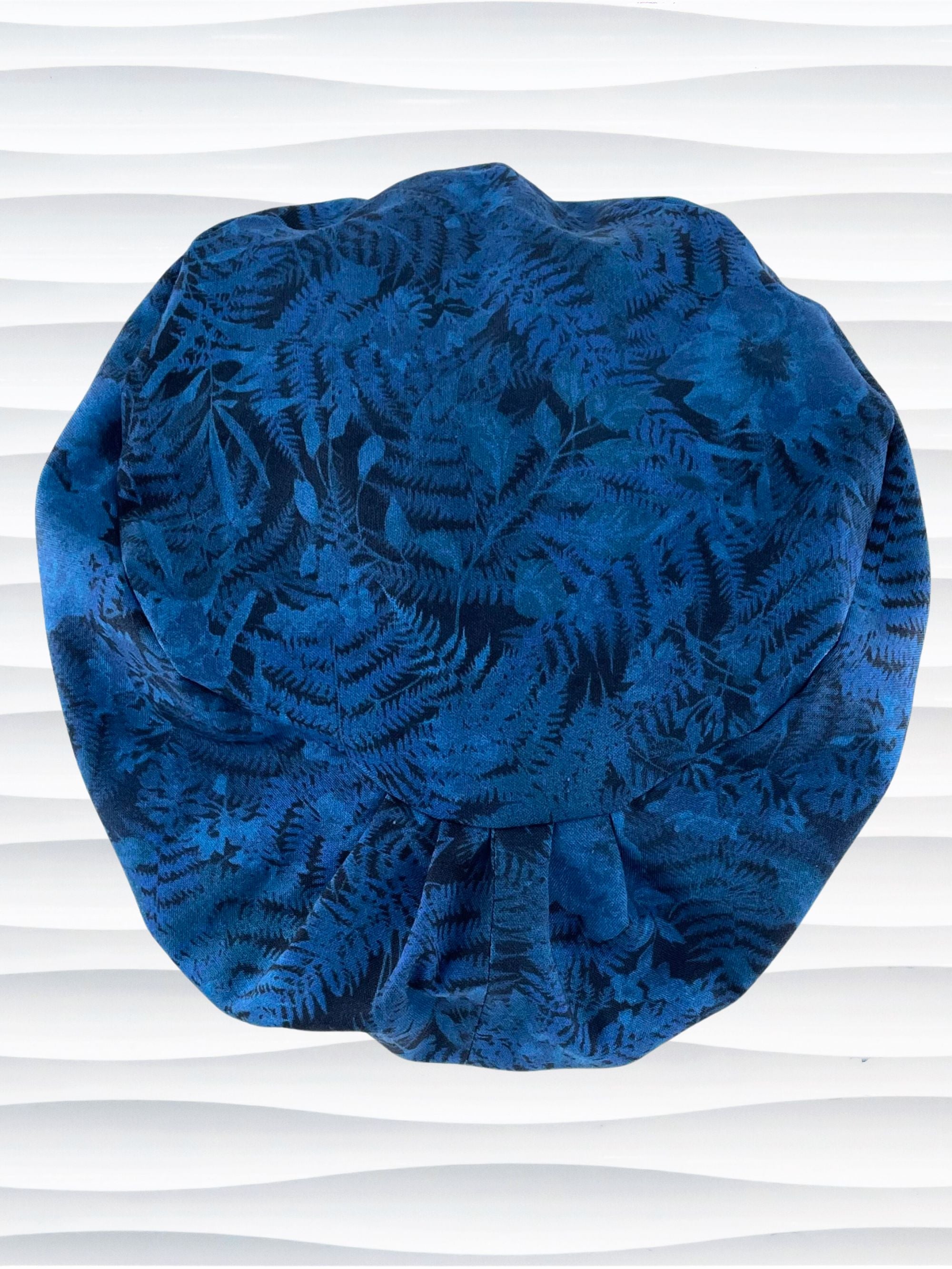 Euro Pixie style surgical scrub cap with a muted pattern of flowers, ferns, and leaves in dark blue on a deep royal blue cotton fabric.