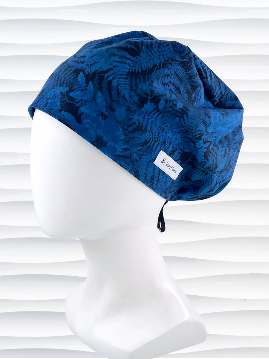 Euro Pixie style surgical scrub cap with a muted pattern of flowers, ferns, and leaves in dark blue on a deep royal blue cotton fabric.