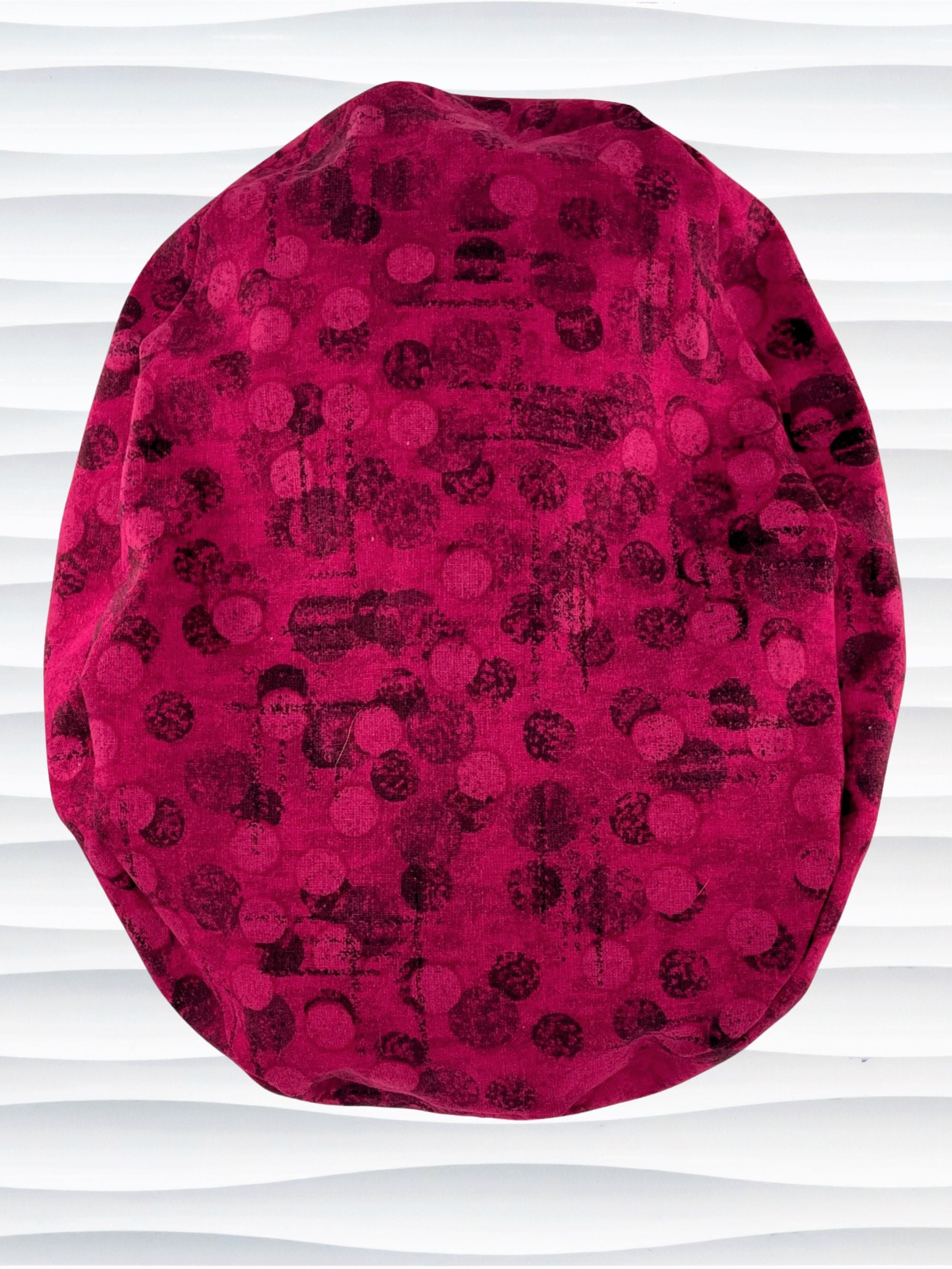 Euro style ponytail surgical scrub cap with a muted pattern of black circles and lines on deep red or magenta cotton fabric.