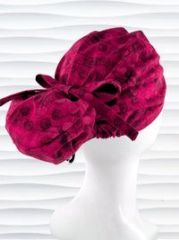 Euro style ponytail surgical scrub cap with a muted pattern of black circles and lines on deep red or magenta cotton fabric.