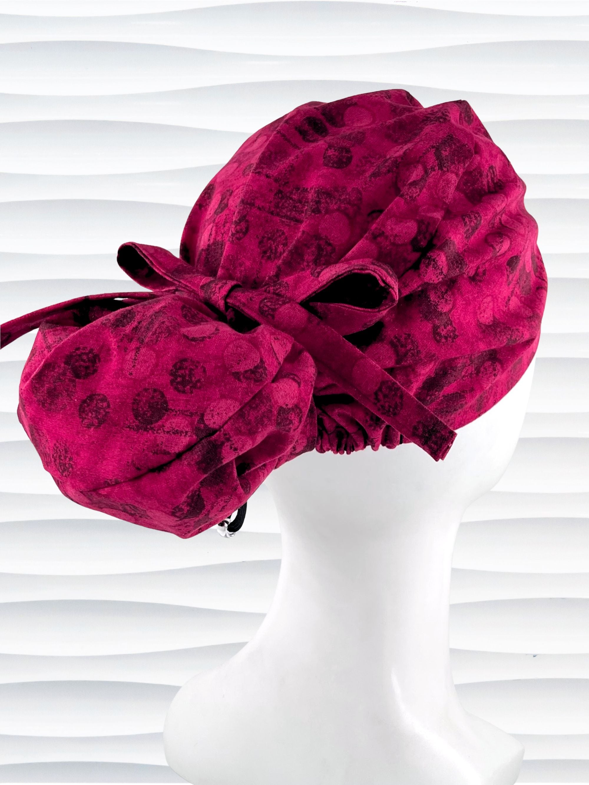 Euro style ponytail surgical scrub cap with a muted pattern of black circles and lines on deep red or magenta cotton fabric.