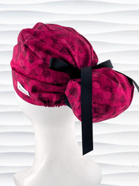 Euro style ponytail surgical scrub cap with a muted pattern of black circles and lines on deep red or magenta cotton fabric.
