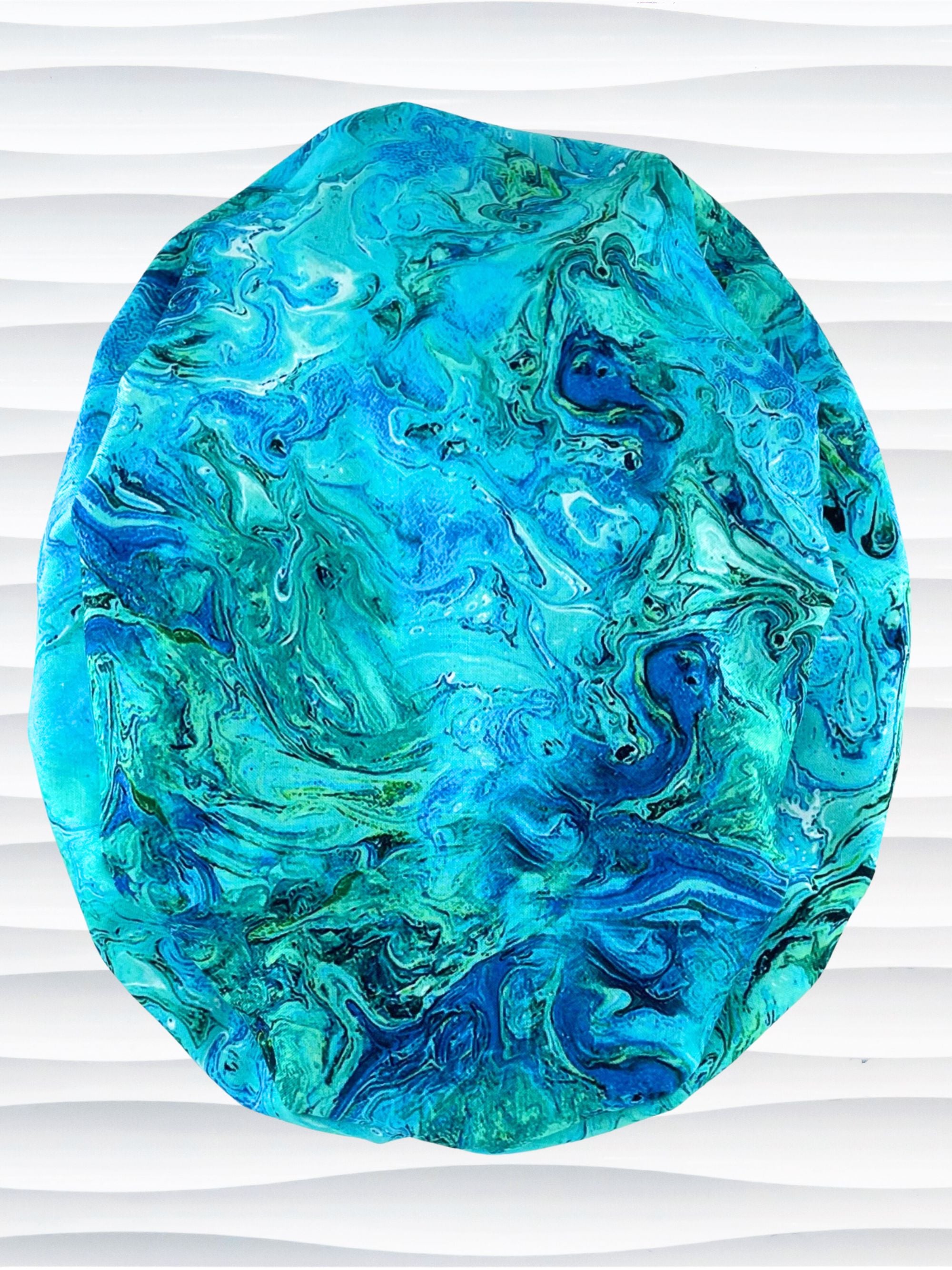 Euro Ponytail surgical scrub cap with a marbled pattern of blues and green that look like ocean tide pools or marbled turquoise on cotton fabric, finished with a tie, and displayed on a white mannequin head.