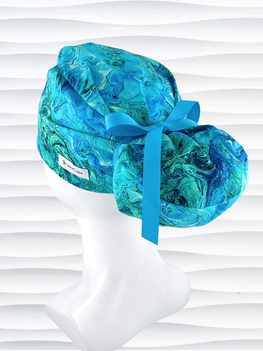Euro Ponytail surgical scrub cap with a marbled pattern of blues and green that look like ocean tide pools or marbled turquoise on cotton fabric, finished with a tie, and displayed on a white mannequin head.
