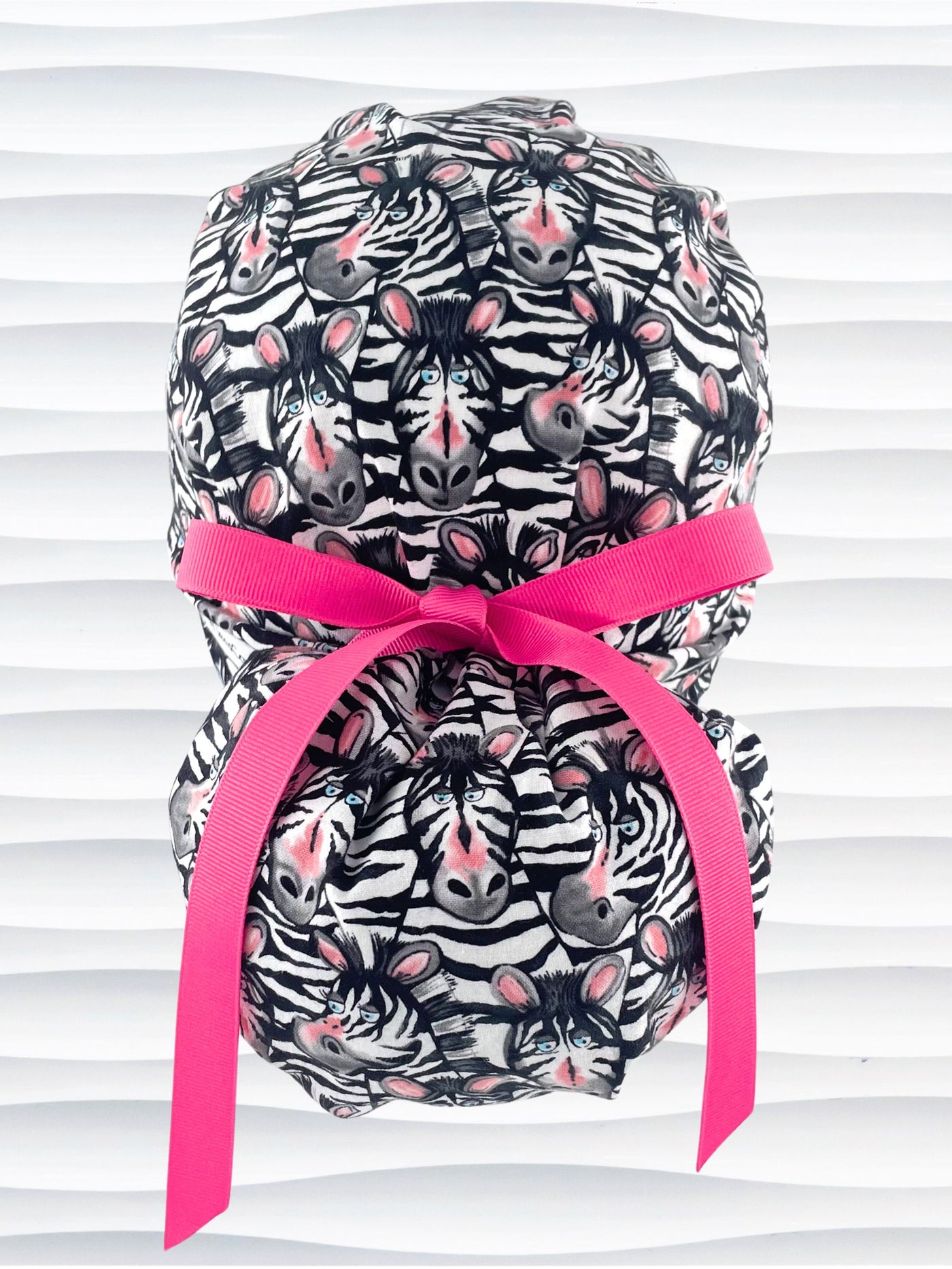 Euro ponytail style surgical scrub cap featuring a black and white zebra print with blue eyes and pink accents with an adjustable back tie and displayed on a mannequin head