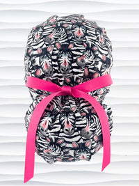 Euro ponytail style surgical scrub cap featuring a black and white zebra print with blue eyes and pink accents with an adjustable back tie and displayed on a mannequin head