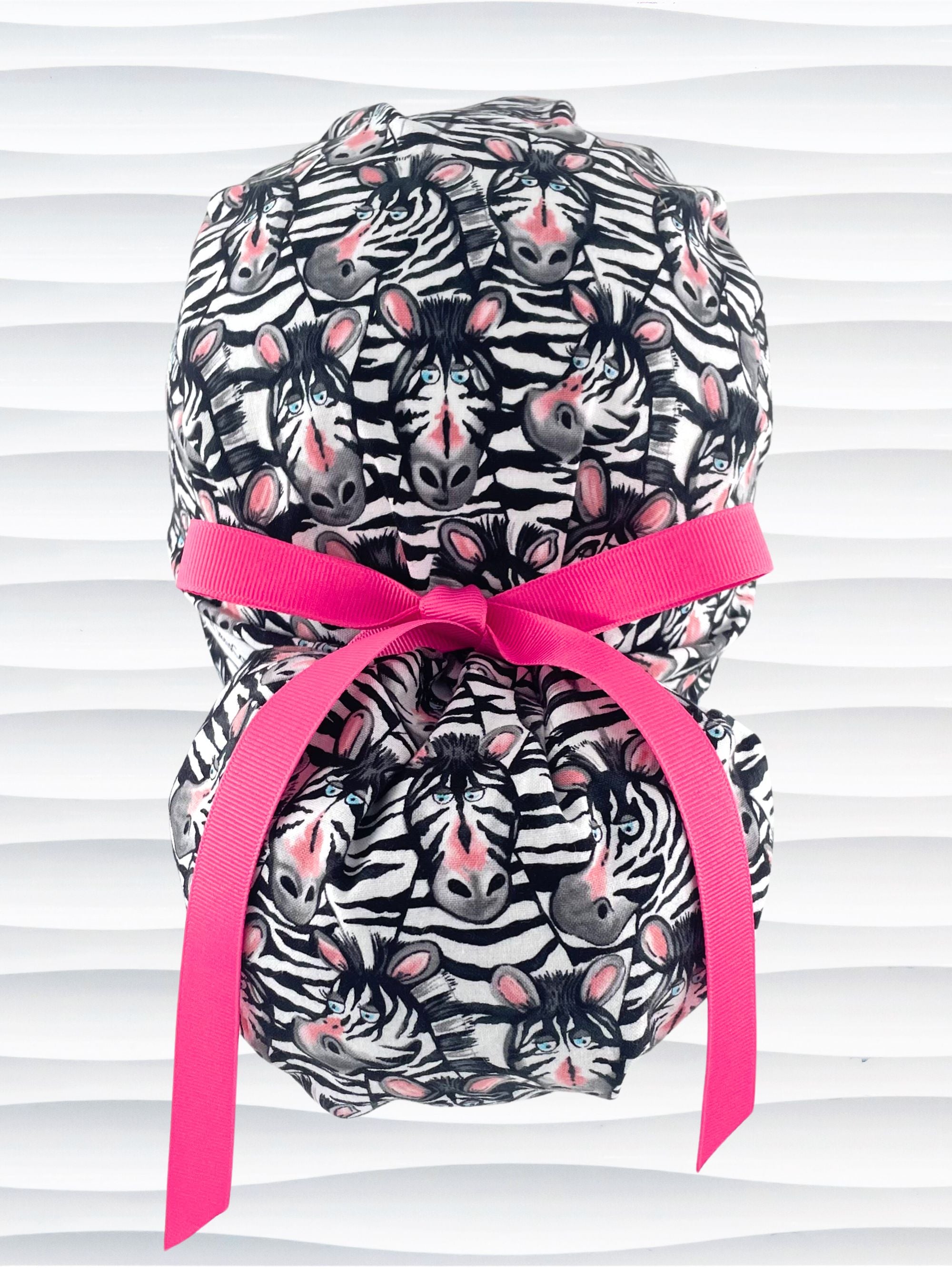 Euro ponytail style surgical scrub cap featuring a black and white zebra print with blue eyes and pink accents with an adjustable back tie and displayed on a mannequin head