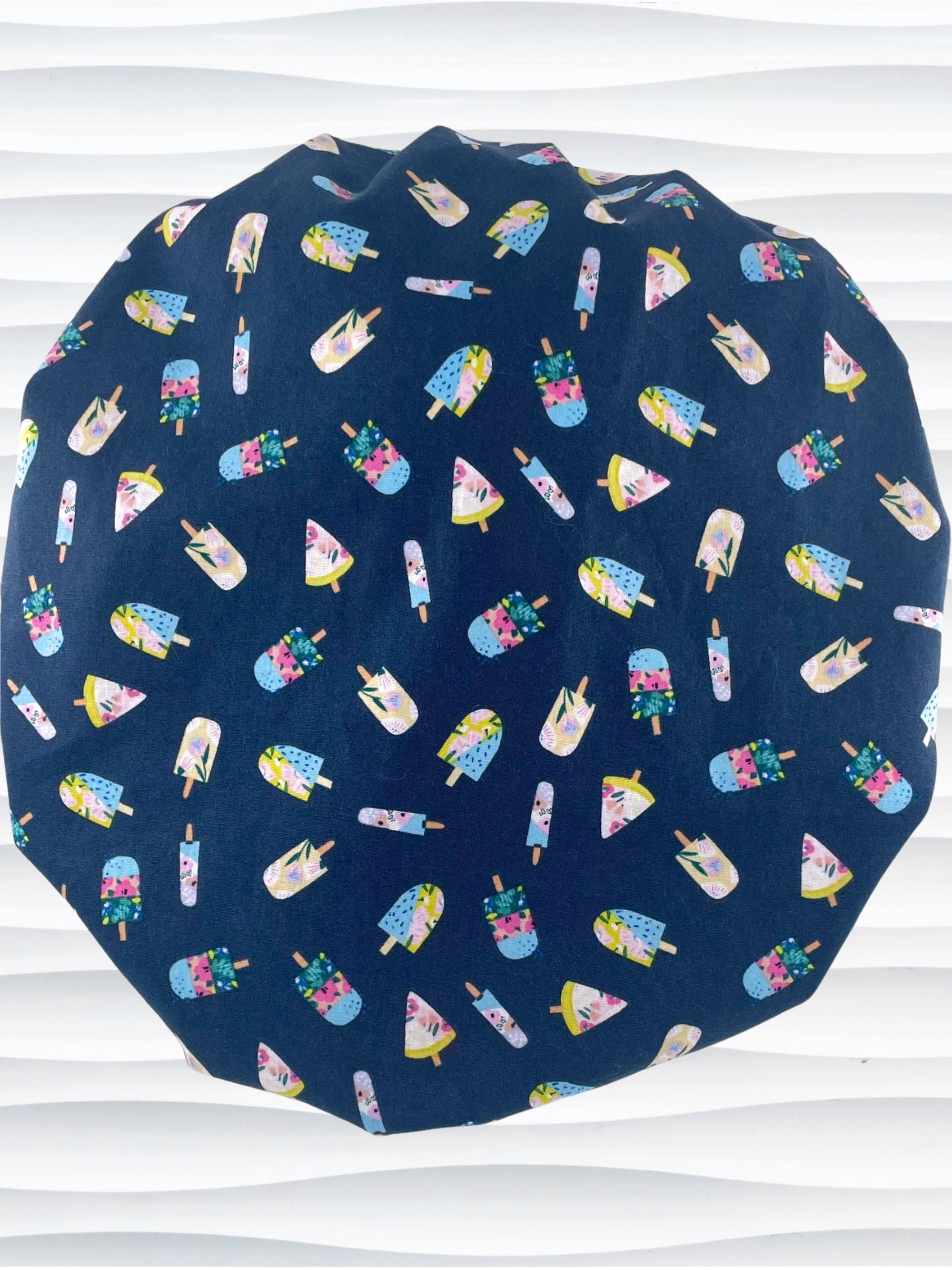 Bouffant style surgical scrub cap backview with popsicles in pink and blue and yellow all over a dark blue cotton fabric.