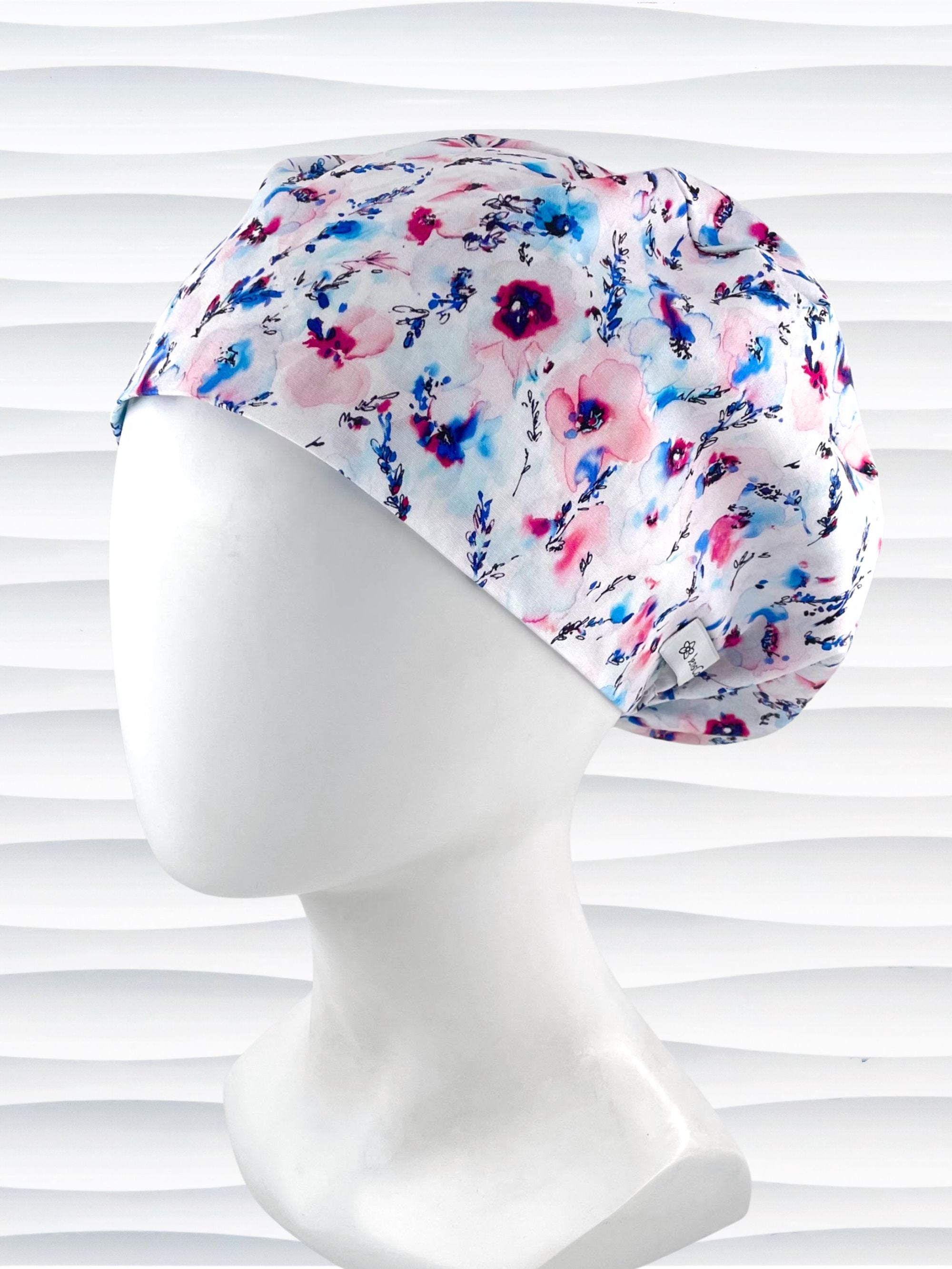Women's euro pixie scrub cap with watercolor floral print in pink, blue, and purple on a white background, ideal for nurses, doctors, and medical professionals seeking stylish and comfortable headwear