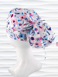 Euro style ponytail surgical scrub cap with abstract flowers in pinks and blues all over white premium cotton fabric and finished with grosgrain ribbon ties.