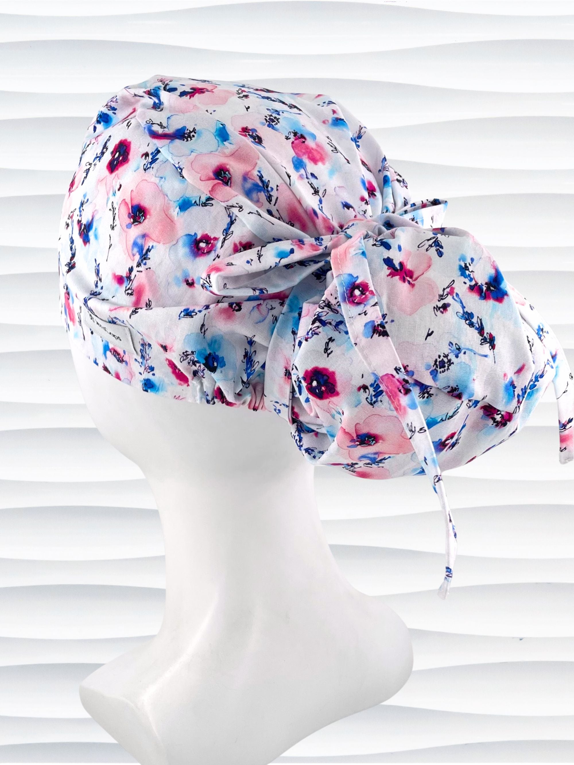 Euro style ponytail surgical scrub cap with abstract flowers in pinks and blues all over white premium cotton fabric and finished with grosgrain ribbon ties.