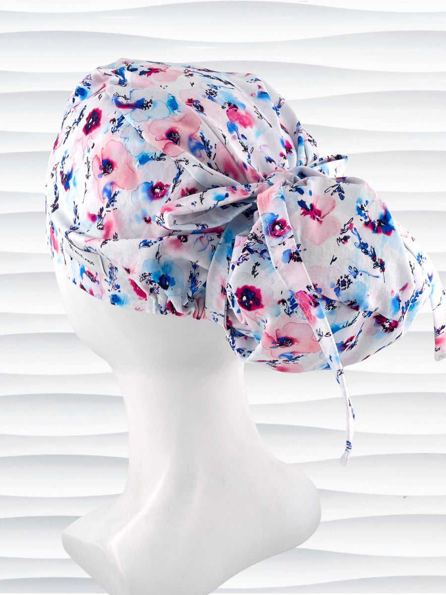 Euro style ponytail surgical scrub cap with abstract flowers in pinks and blues all over white premium cotton fabric and finished with grosgrain ribbon ties.