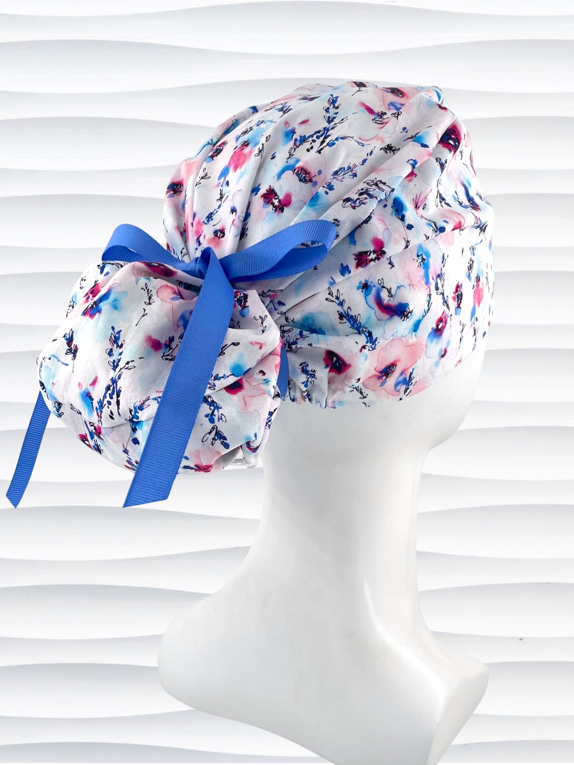 Euro style ponytail surgical scrub cap with abstract flowers in pinks and blues all over white premium cotton fabric and finished with grosgrain ribbon ties.
