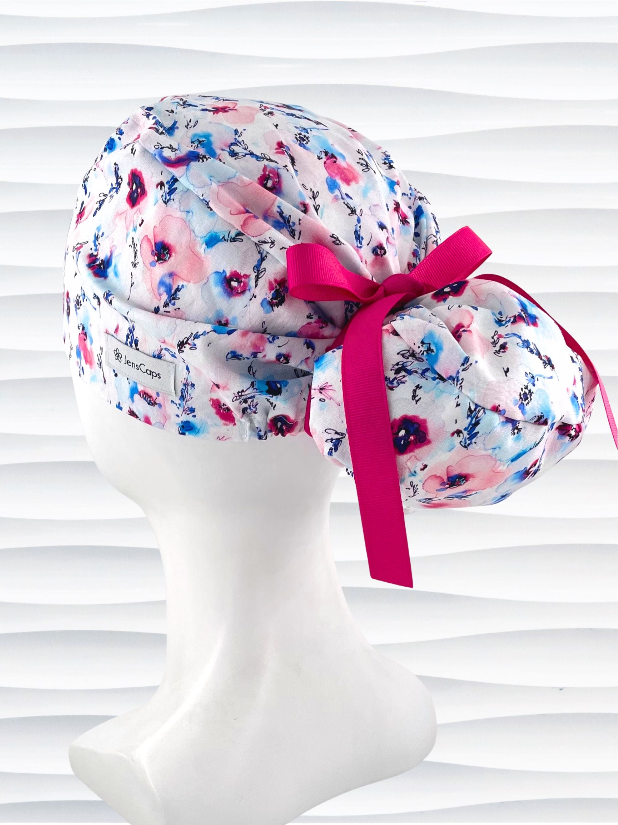Euro style ponytail surgical scrub cap with abstract flowers in pinks and blues all over white premium cotton fabric and finished with grosgrain ribbon ties.