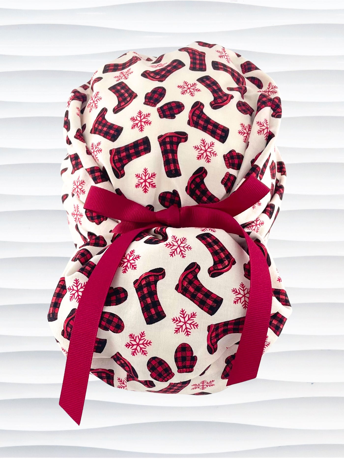 Euro Pony style surgical scrub cap with red snowflakes and red and black buffalo check boots and mittens tossed all over this ivory background on cotton fabric  and finished with a grosgrain ribbon tie.