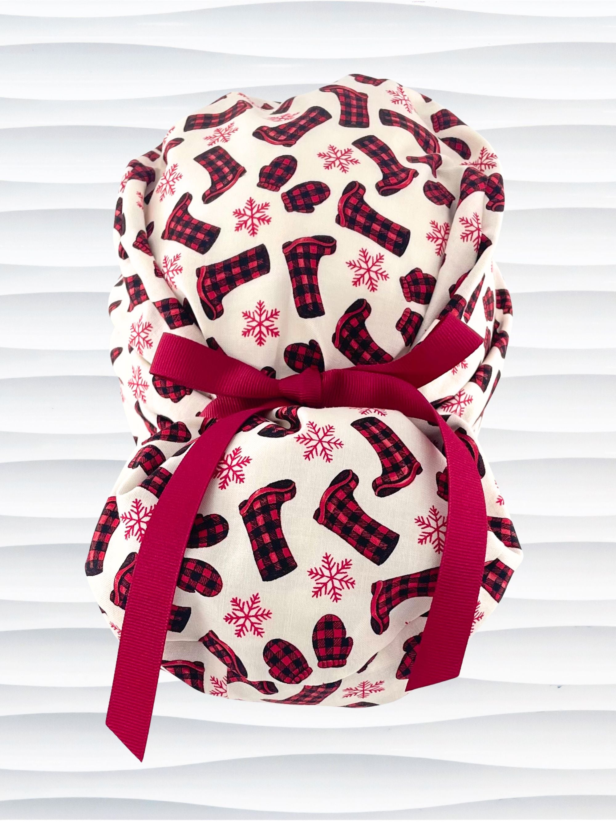 Euro Pony style surgical scrub cap with red snowflakes and red and black buffalo check boots and mittens tossed all over this ivory background on cotton fabric  and finished with a grosgrain ribbon tie.