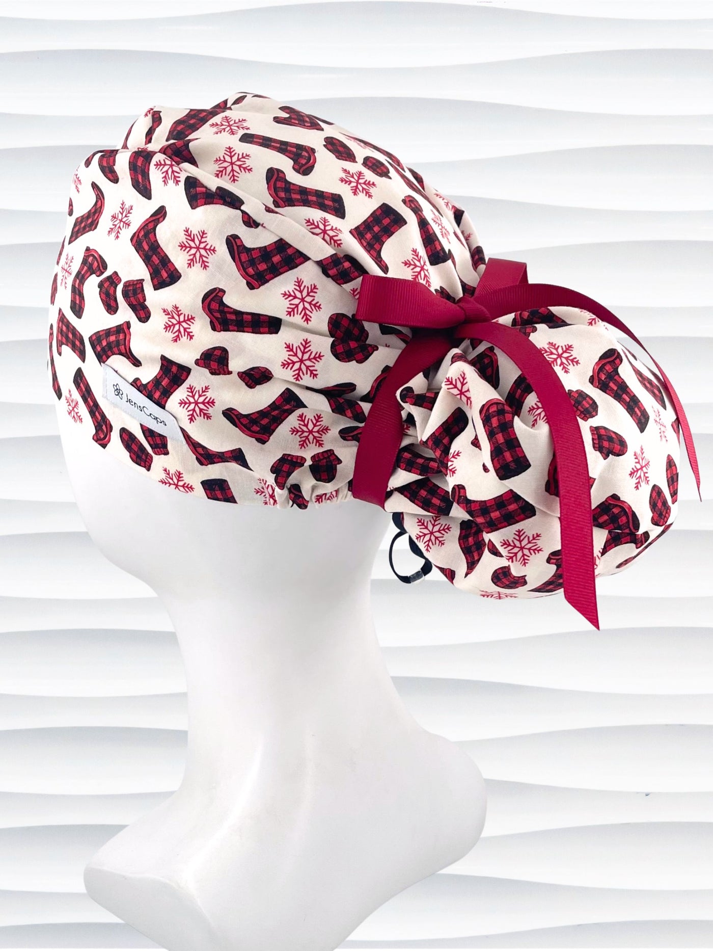 Euro Pony style surgical scrub cap with red snowflakes and red and black buffalo check boots and mittens tossed all over this ivory background on cotton fabric  and finished with a grosgrain ribbon tie.