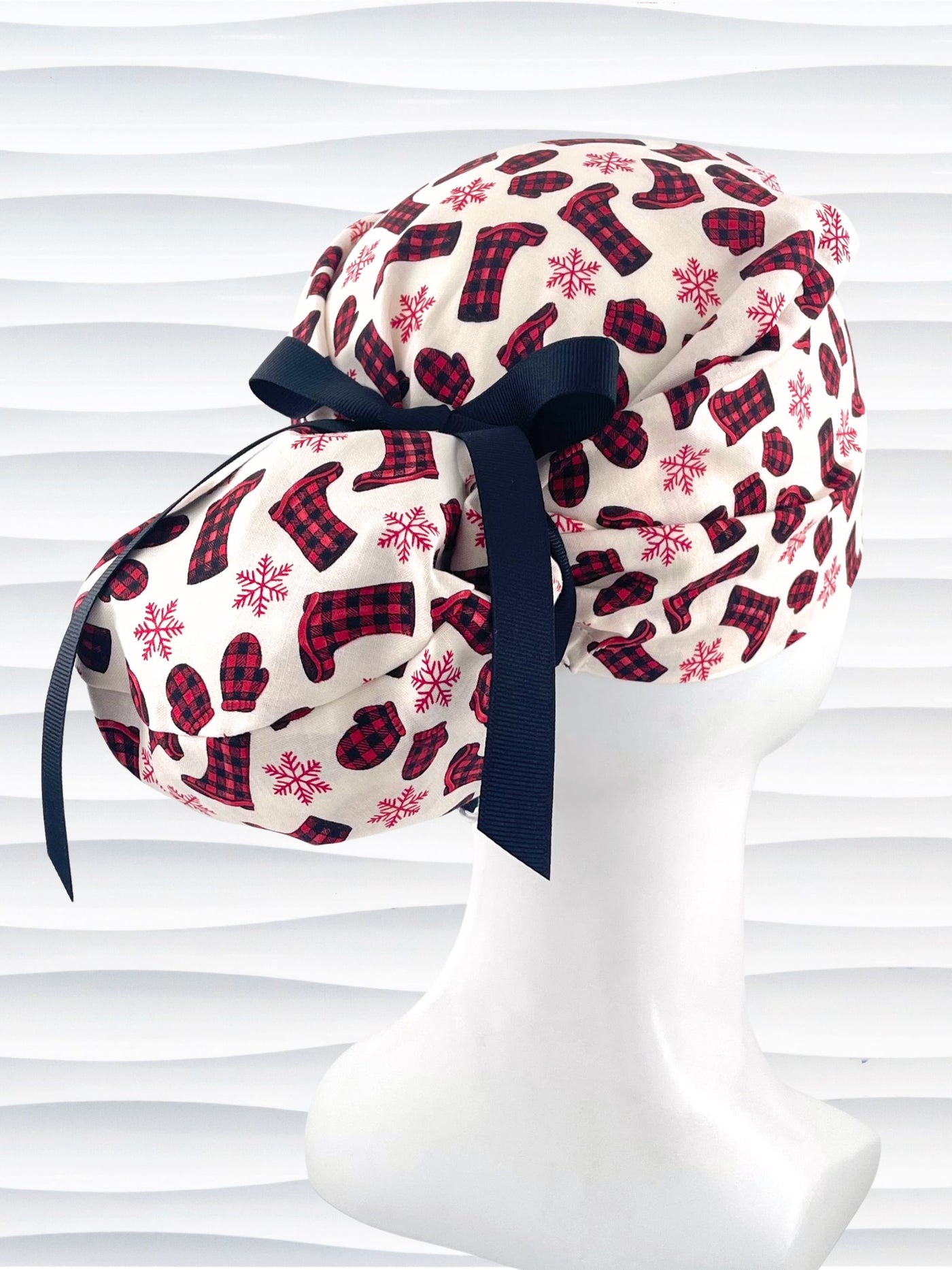 Euro Pony style surgical scrub cap with red snowflakes and red and black buffalo check boots and mittens tossed all over this ivory background on cotton fabric  and finished with a grosgrain ribbon tie.