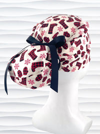 Euro Pony style surgical scrub cap with red snowflakes and red and black buffalo check boots and mittens tossed all over this ivory background on cotton fabric  and finished with a grosgrain ribbon tie.