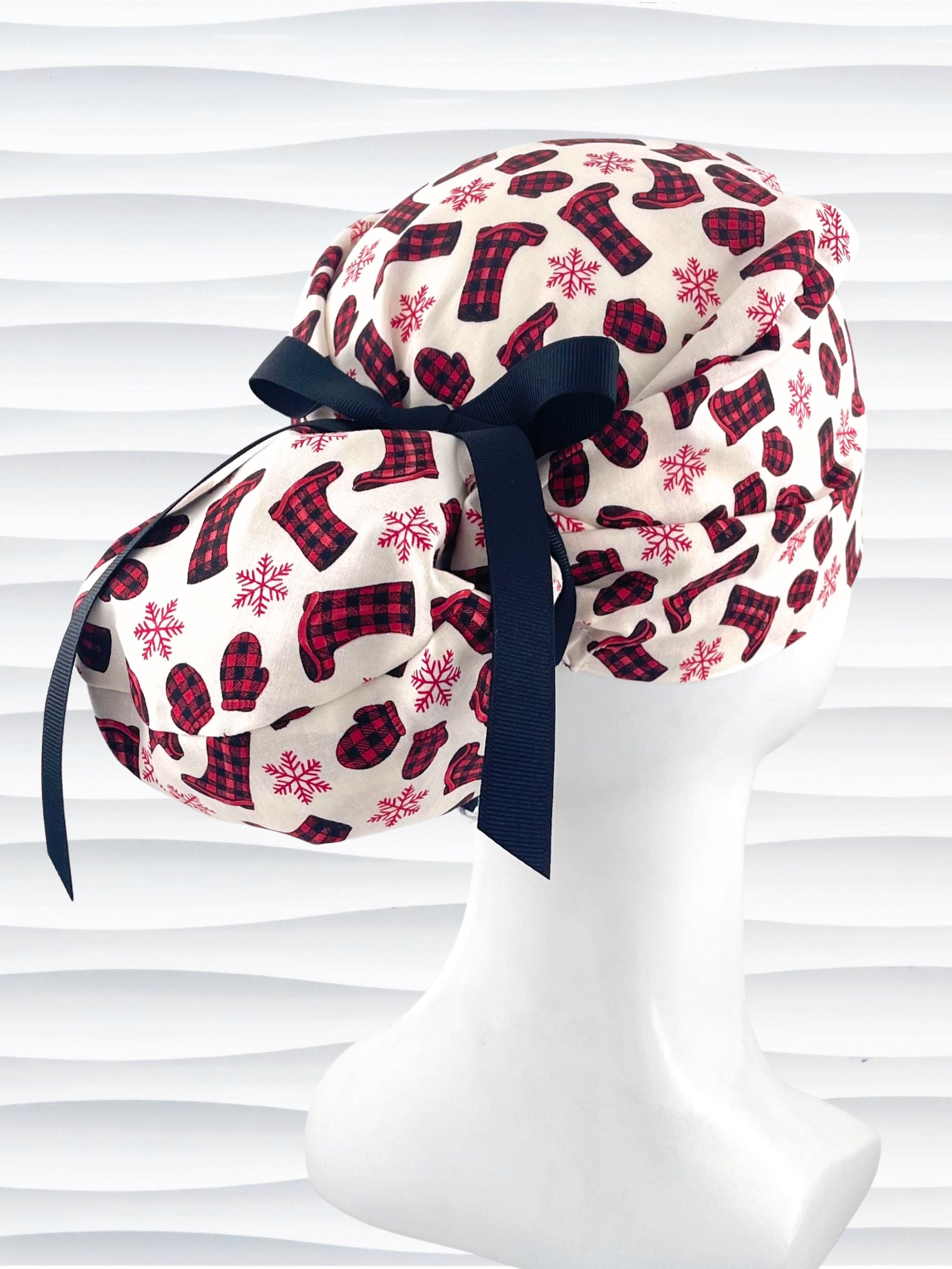 Euro Pony style surgical scrub cap with red snowflakes and red and black buffalo check boots and mittens tossed all over this ivory background on cotton fabric  and finished with a grosgrain ribbon tie.