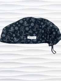 Euro Pixie style surgical scrub cap by JensCaps with silver outlines of lemons, lemon leaves, and lemon slices all over a black background and displayed on a white mannequin head.