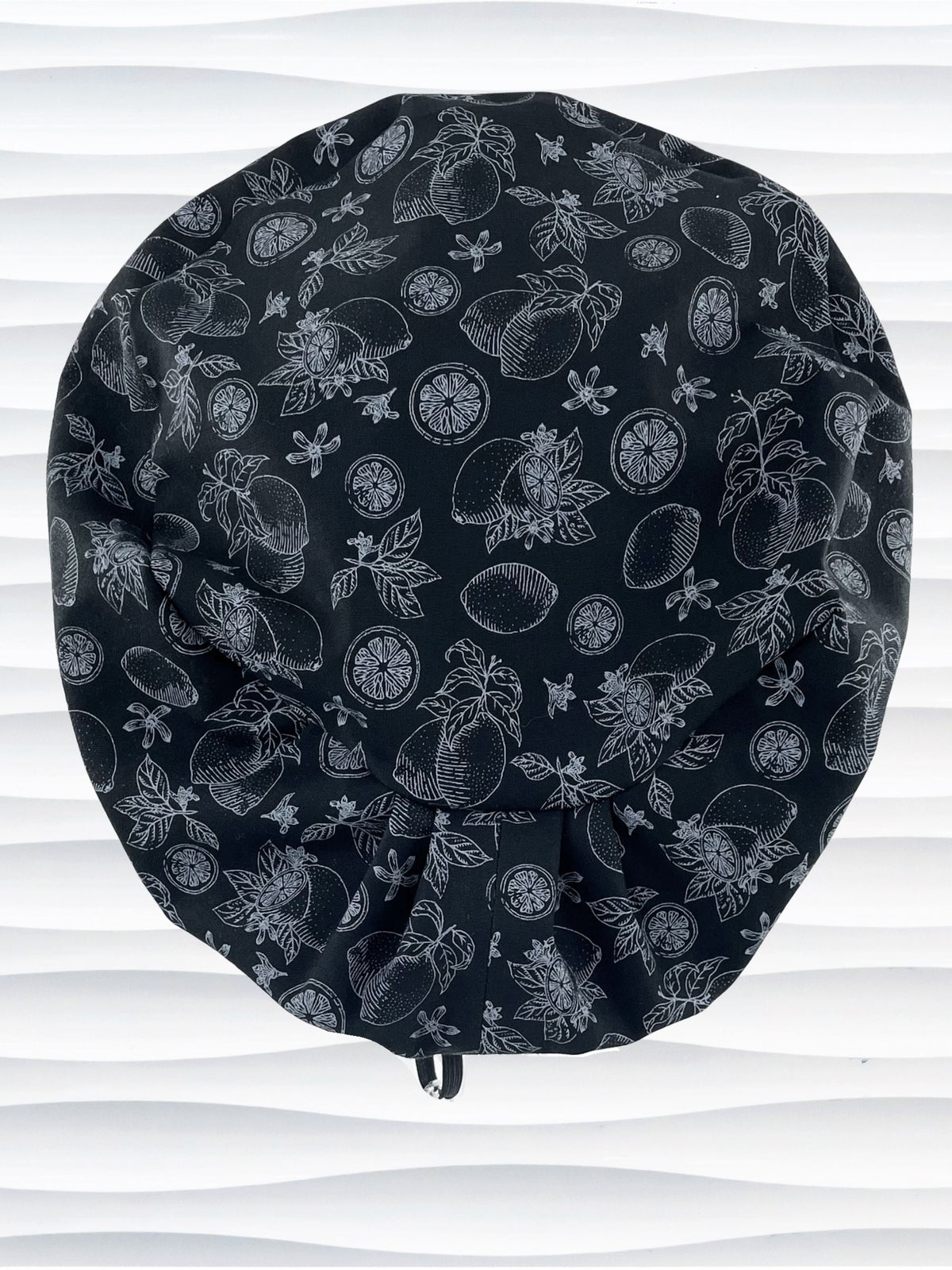 Euro Pixie style surgical scrub cap by JensCaps with silver outlines of lemons, lemon leaves, and lemon slices all over a black background and displayed on a white mannequin head.