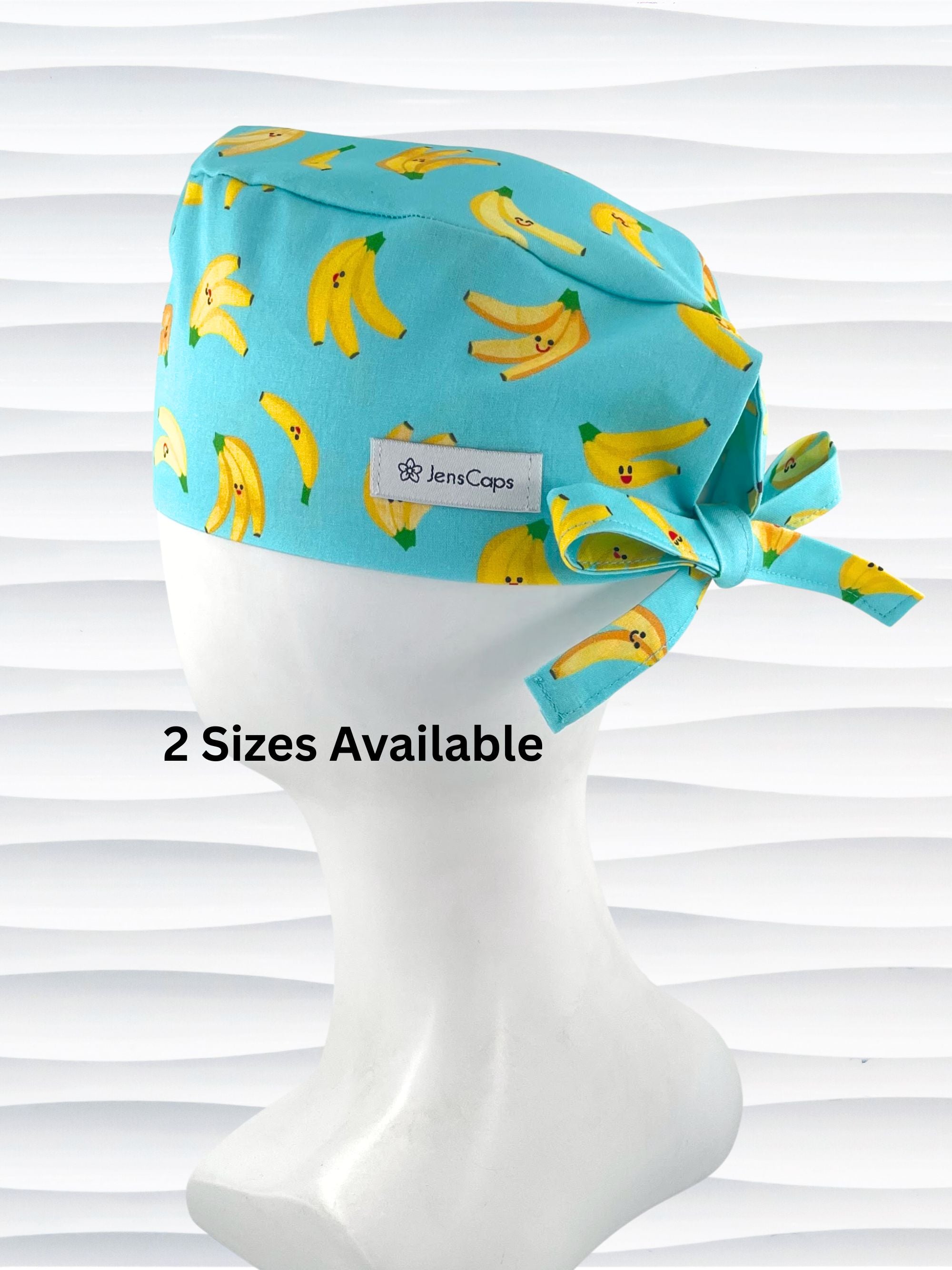 Mens style surgical scrub cap with bright yellow bananas tossed on this vibrant blue cotton fabric and finished with adjustable ties shown on mannequin head with a white textured background.