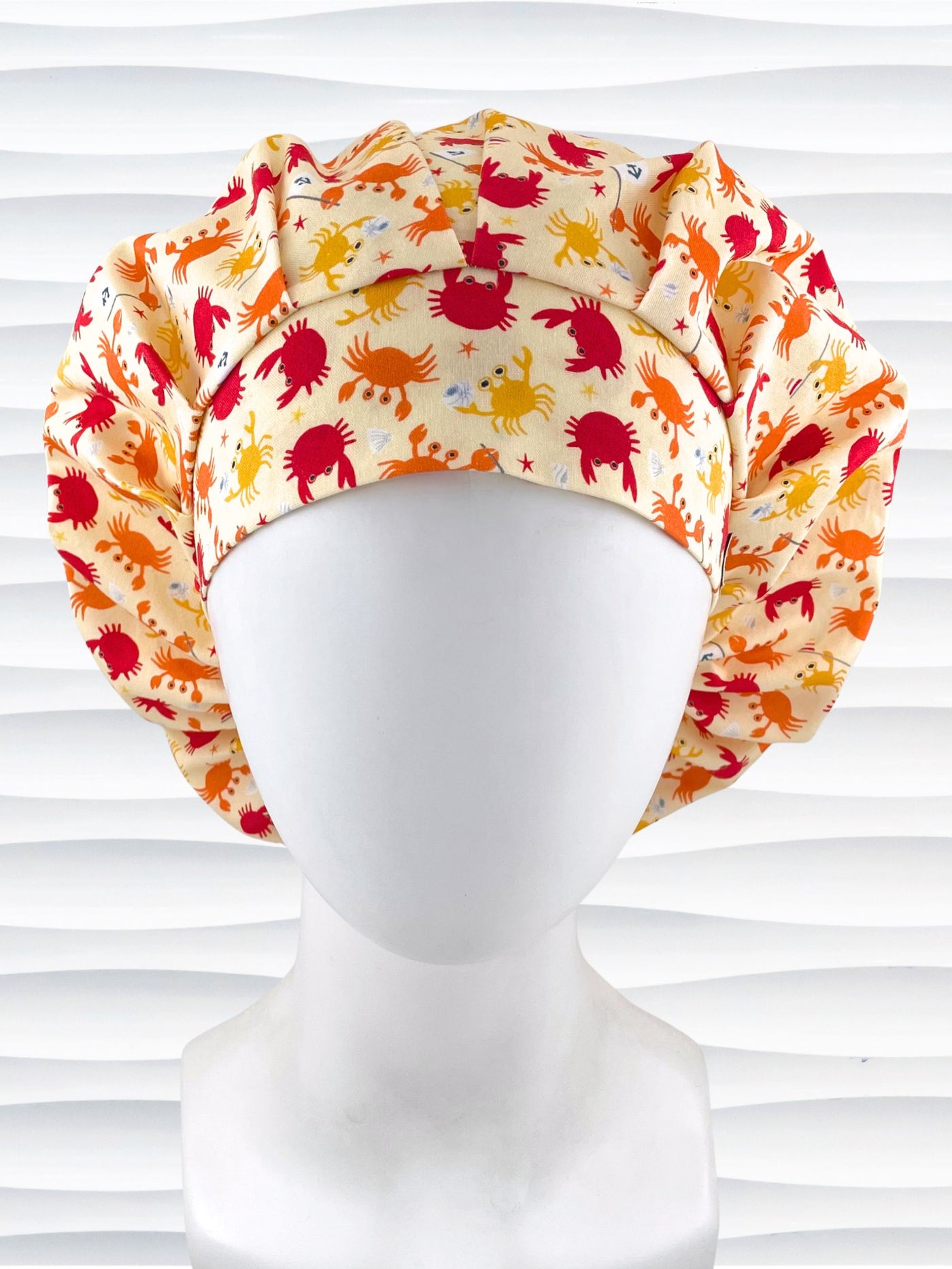 Colorful crab print surgical scrub cap featuring orange, red, and yellow cartoon crabs on cream fabric, displayed on mannequin head – handmade nurse and doctor scrub hat by JensCaps