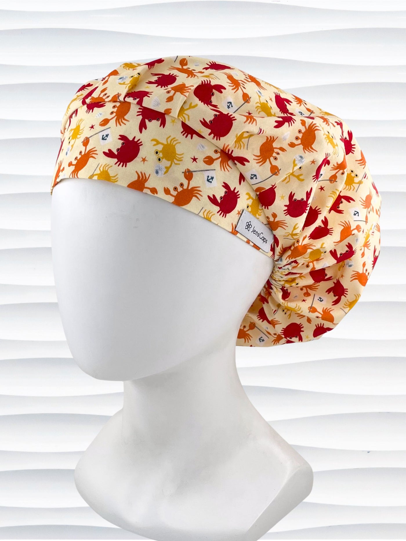 Colorful crab print surgical scrub cap featuring orange, red, and yellow cartoon crabs on cream fabric, displayed on mannequin head – handmade nurse and doctor scrub hat by JensCaps