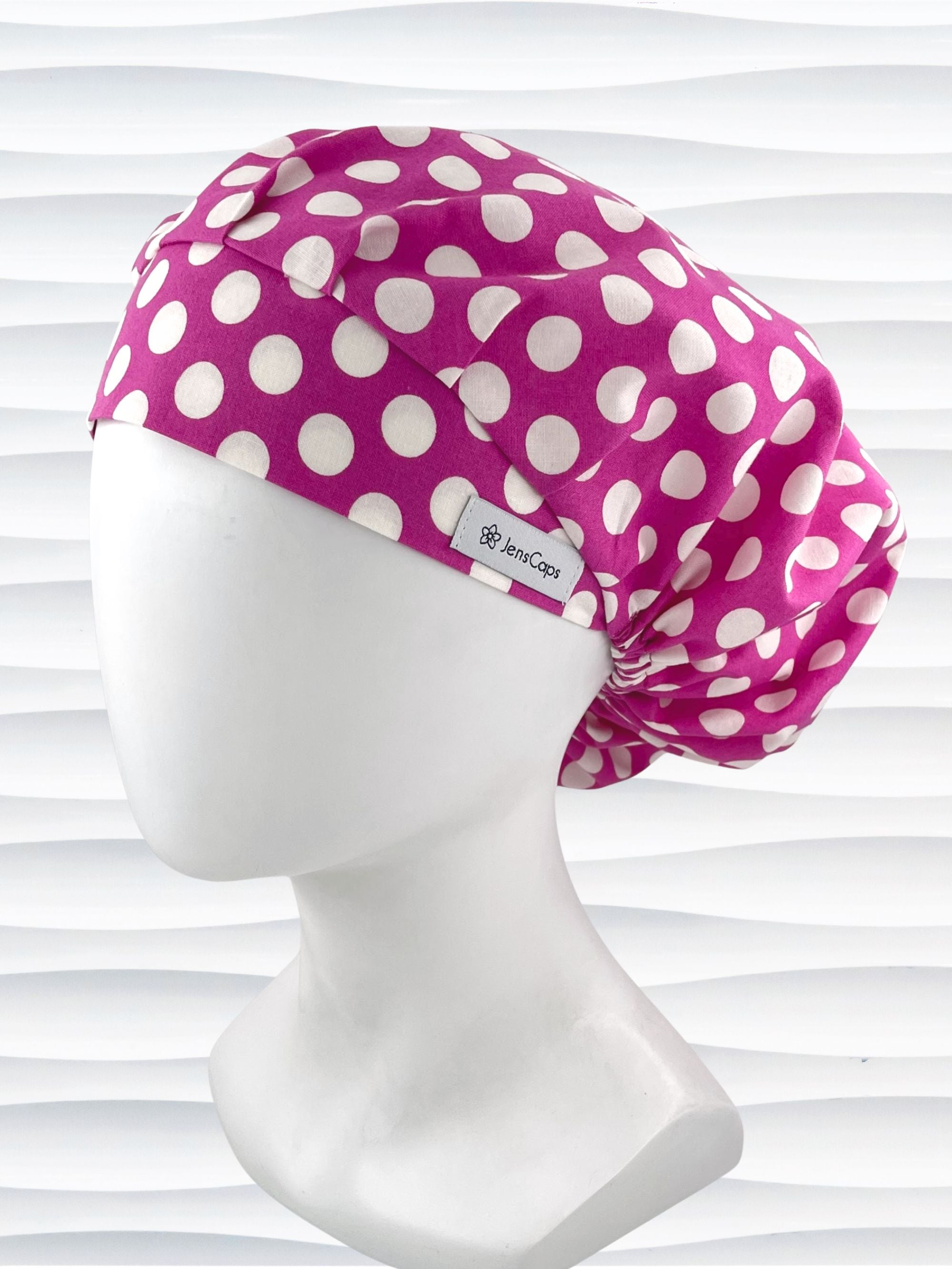 Bouffant style surgical scrub cap by JensCaps with large white dots on raspberry colored cotton fabric.