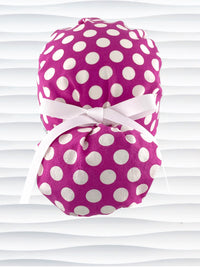 Ponytail style surgical scrub cap by JensCaps with large white retro inspired polka dots on a rasberry colored cotton fabric, and finished with a ribbon tie.