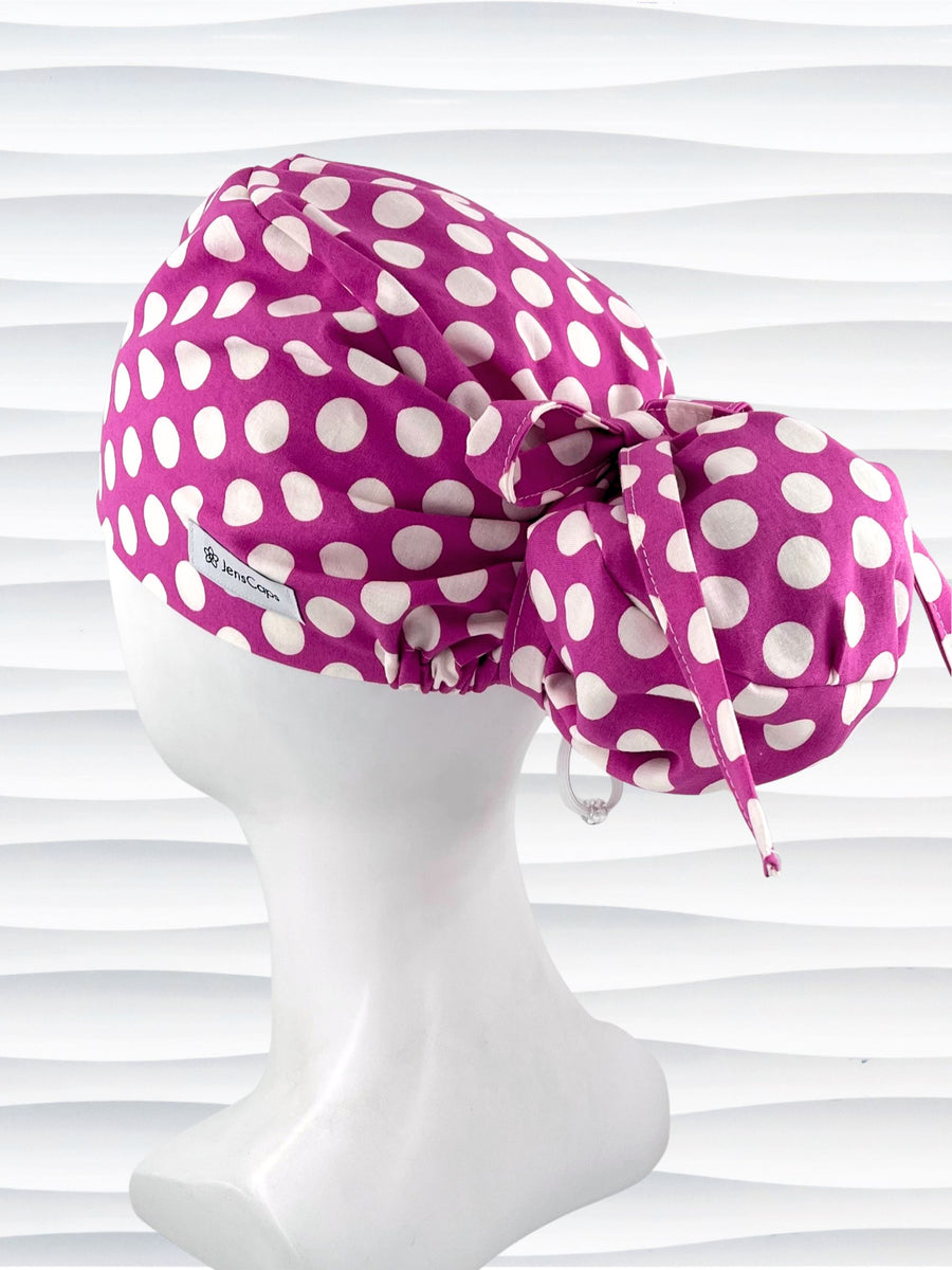 Euro Pony style ponytail surgical scrub cap by JensCaps with large white dots on raspberry colored cotton fabric.