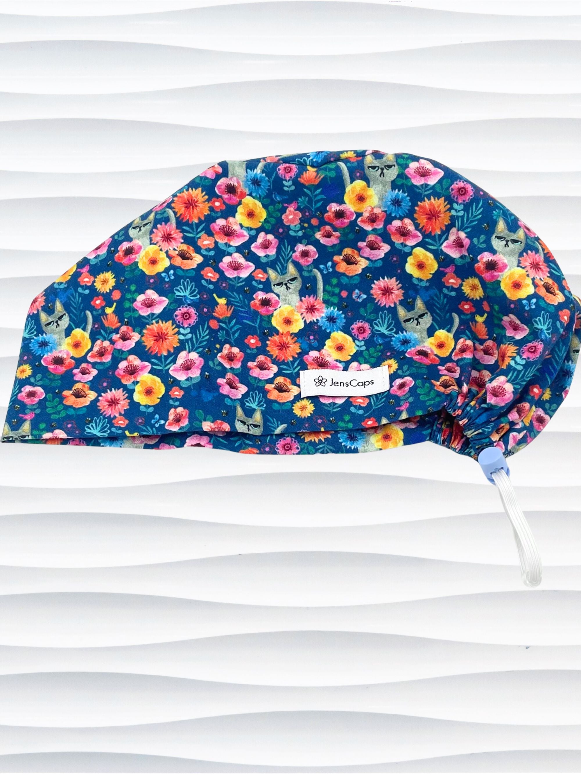 Euro Pixie style surgical scrub cap by JensCaps with gray cats hiding in a garden of yellow, pink, and red flowers on a dark blue cotton fabric