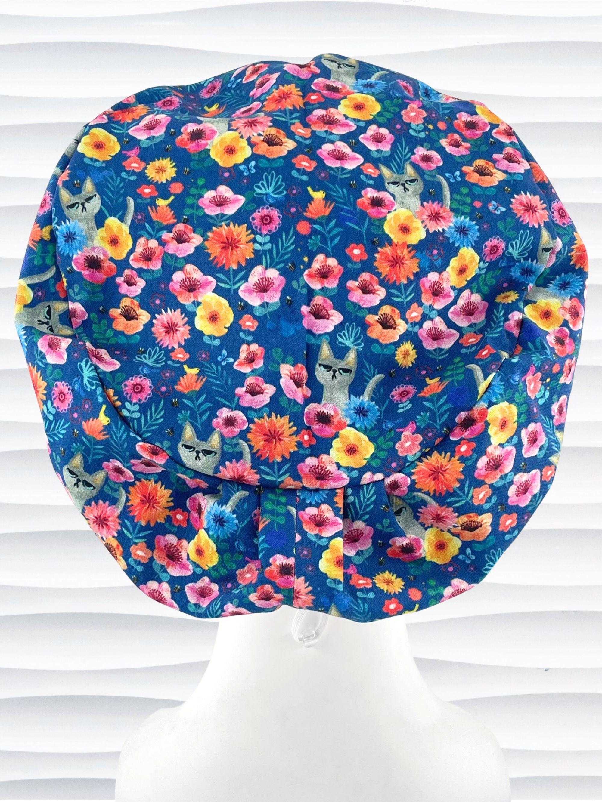 Euro Pixie style surgical scrub cap by JensCaps with gray cats hiding in a garden of yellow, pink, and red flowers on a dark blue cotton fabric