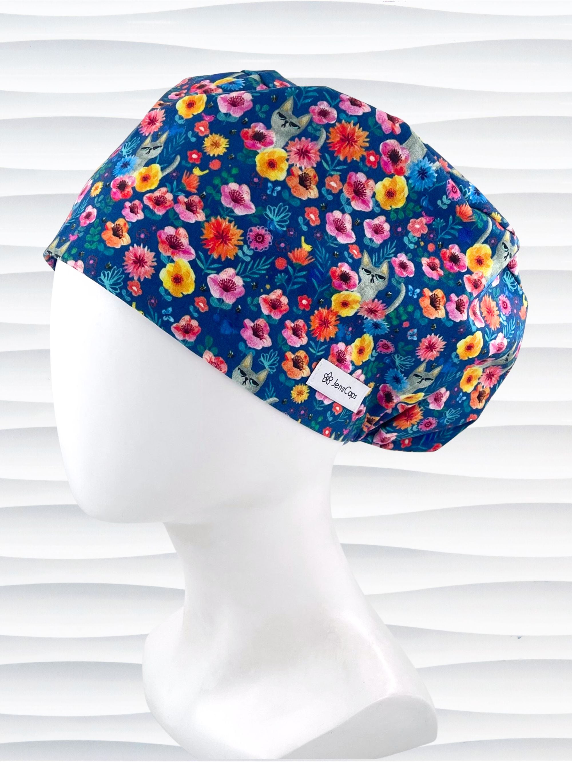Euro Pixie style surgical scrub cap by JensCaps with gray cats hiding in a garden of yellow, pink, and red flowers on a dark blue cotton fabric