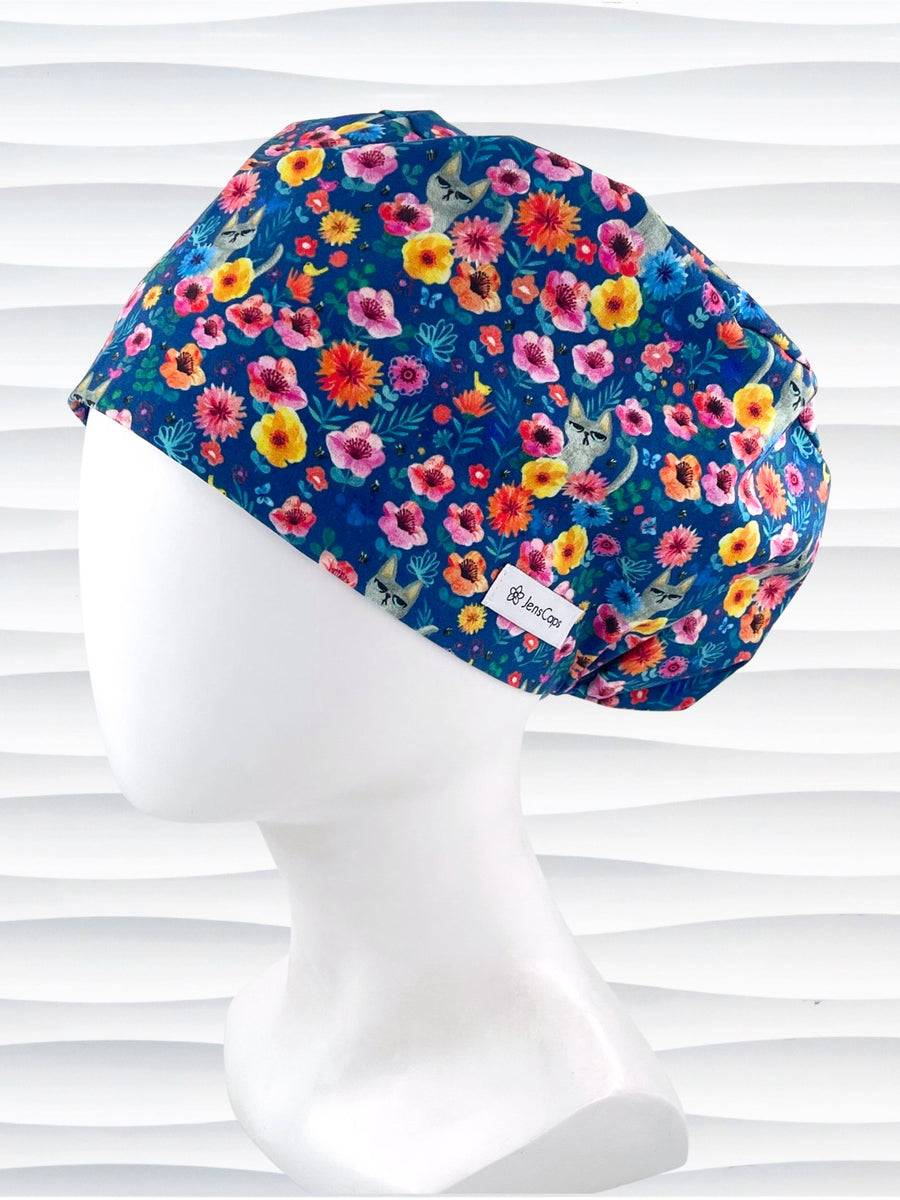 Euro Pixie style surgical scrub cap by JensCaps with gray cats hiding in a garden of yellow, pink, and red flowers on a dark blue cotton fabric