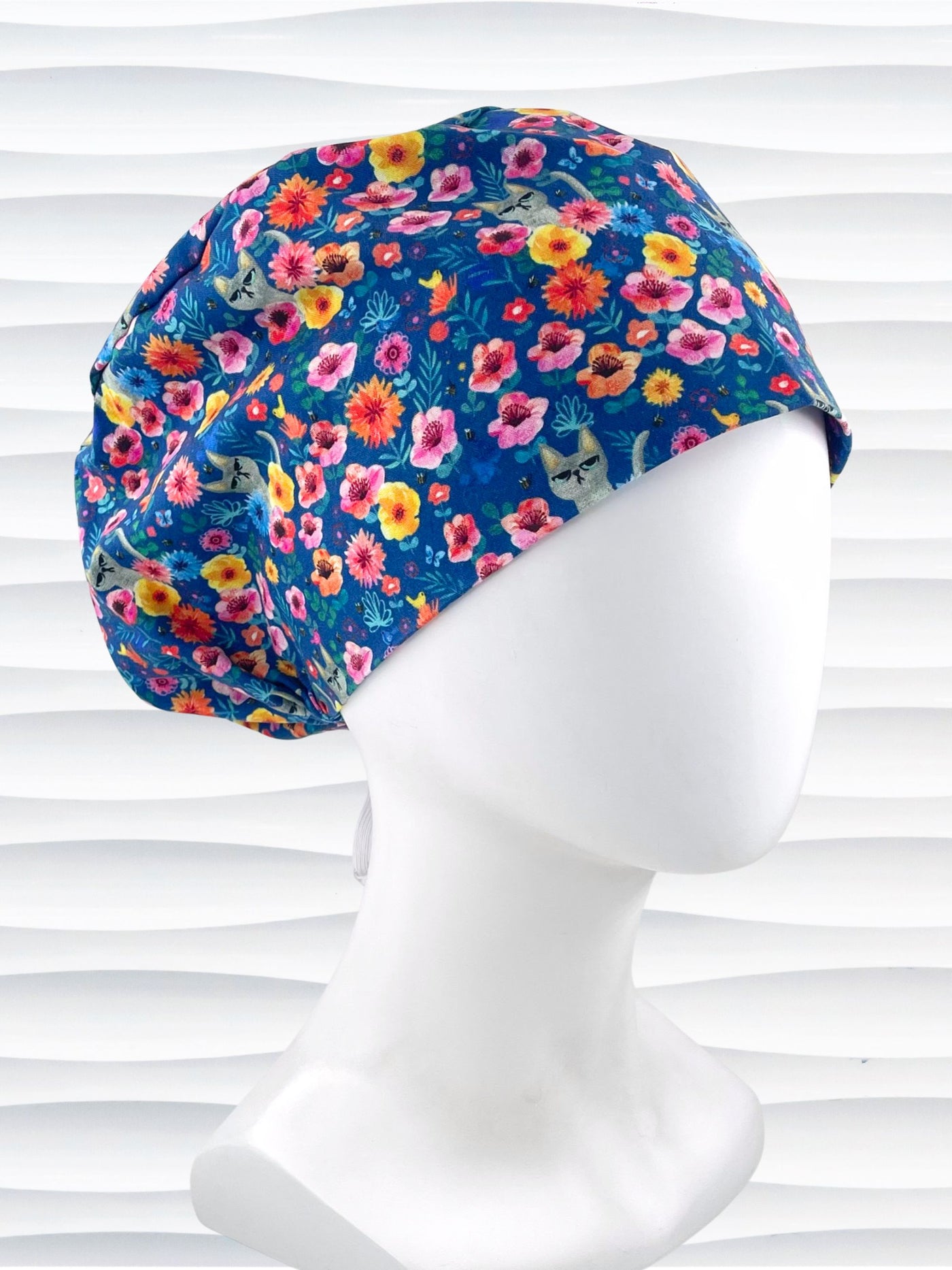 Euro Pixie style surgical scrub cap by JensCaps with gray cats hiding in a garden of yellow, pink, and red flowers on a dark blue cotton fabric