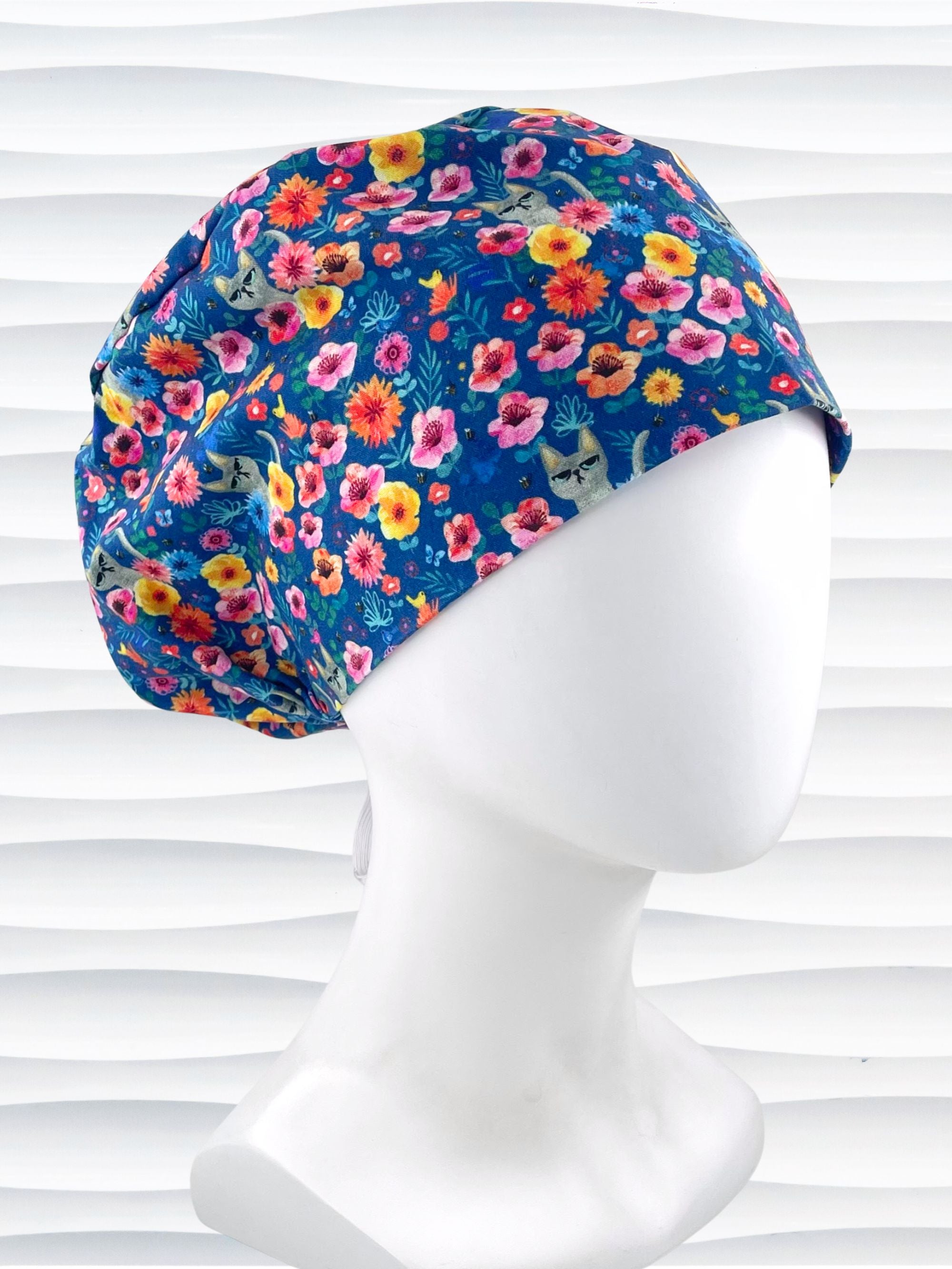 Euro Pixie style surgical scrub cap by JensCaps with gray cats hiding in a garden of yellow, pink, and red flowers on a dark blue cotton fabric