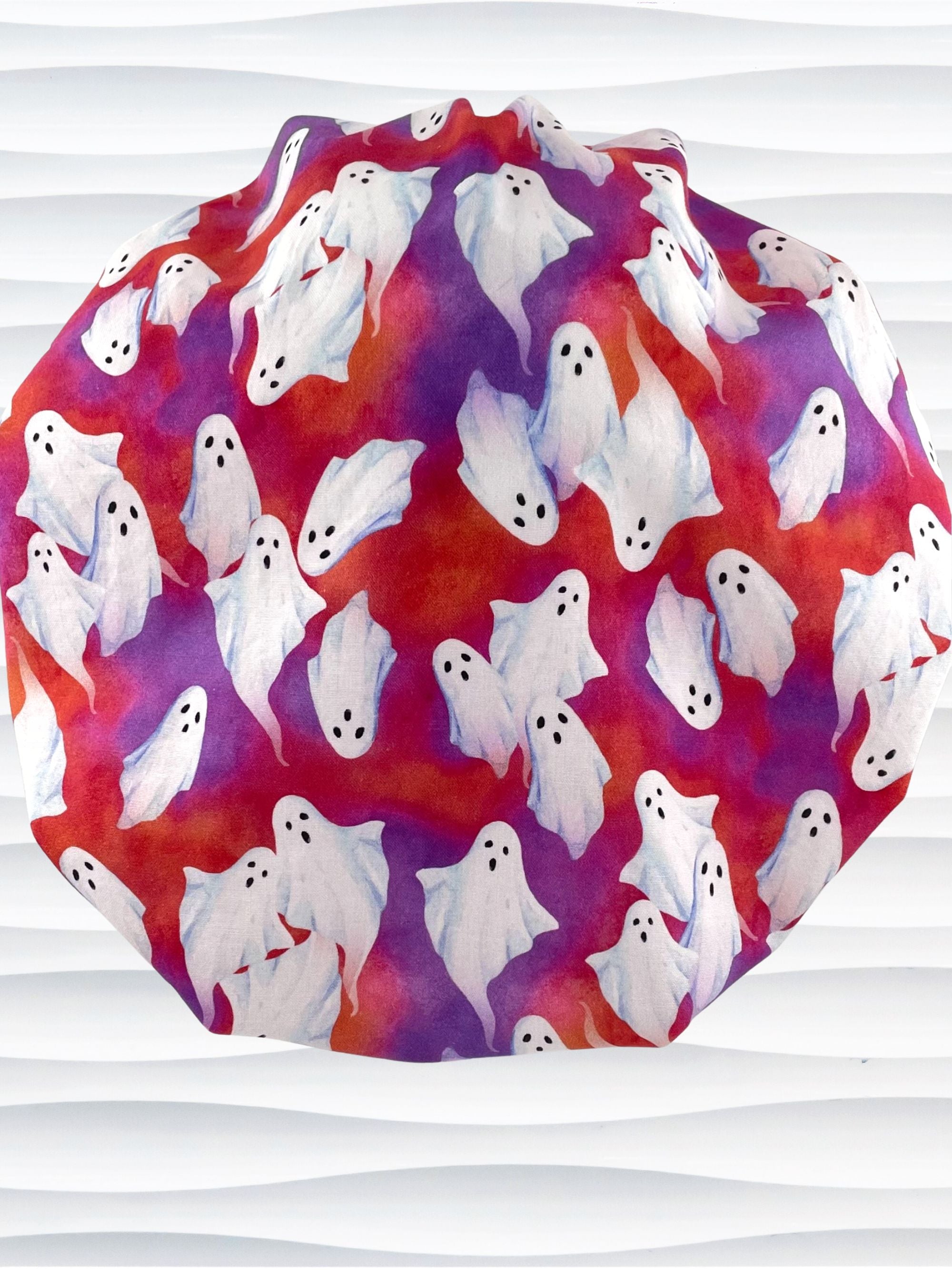 Bouffant style surgical scrub cap by JensCaps with white sheet ghosts tossed all aver an ombre red and purple cotton fabric.