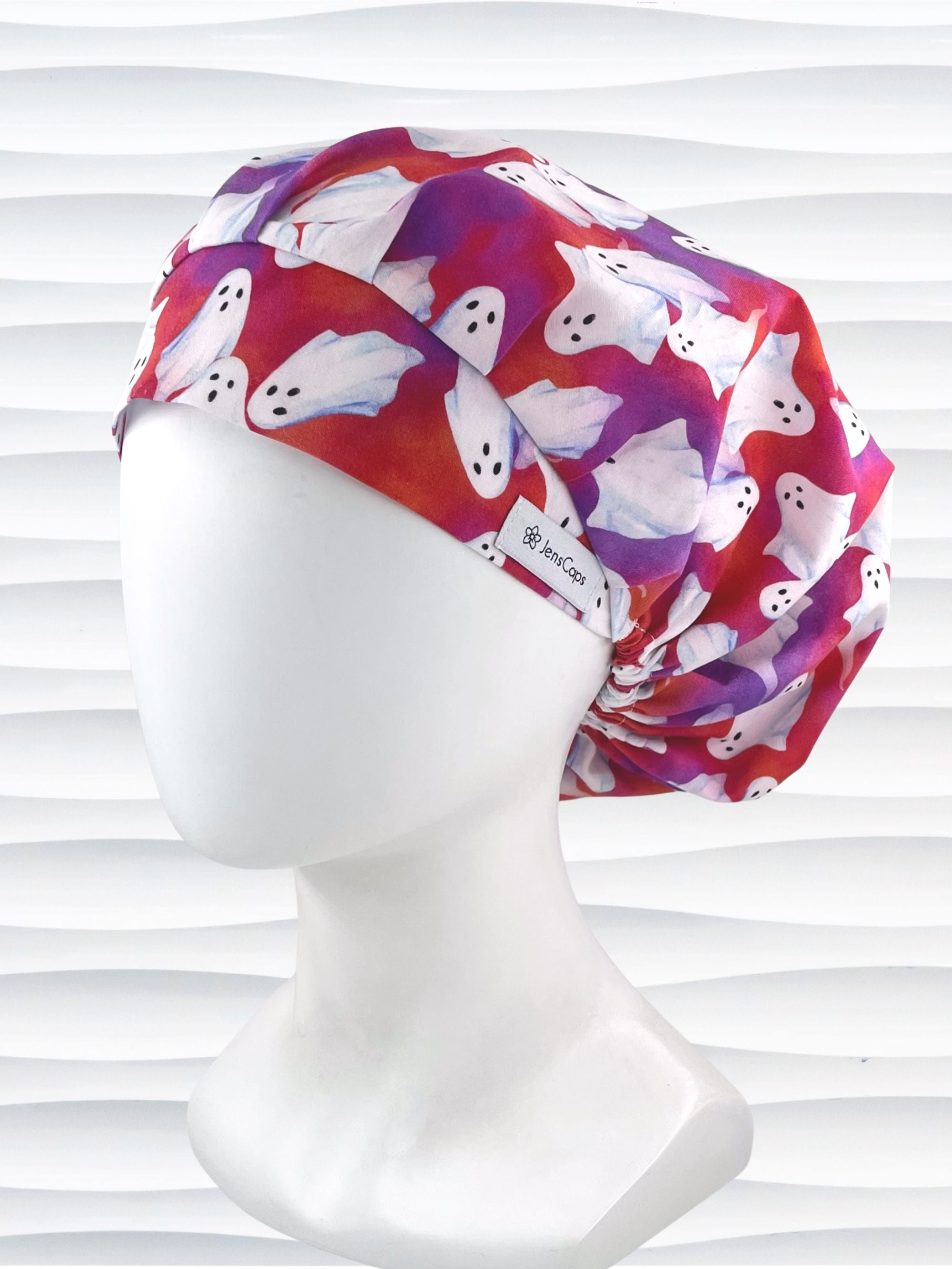 Bouffant style surgical scrub cap by JensCaps with white sheet ghosts tossed all aver an ombre red and purple cotton fabric.
