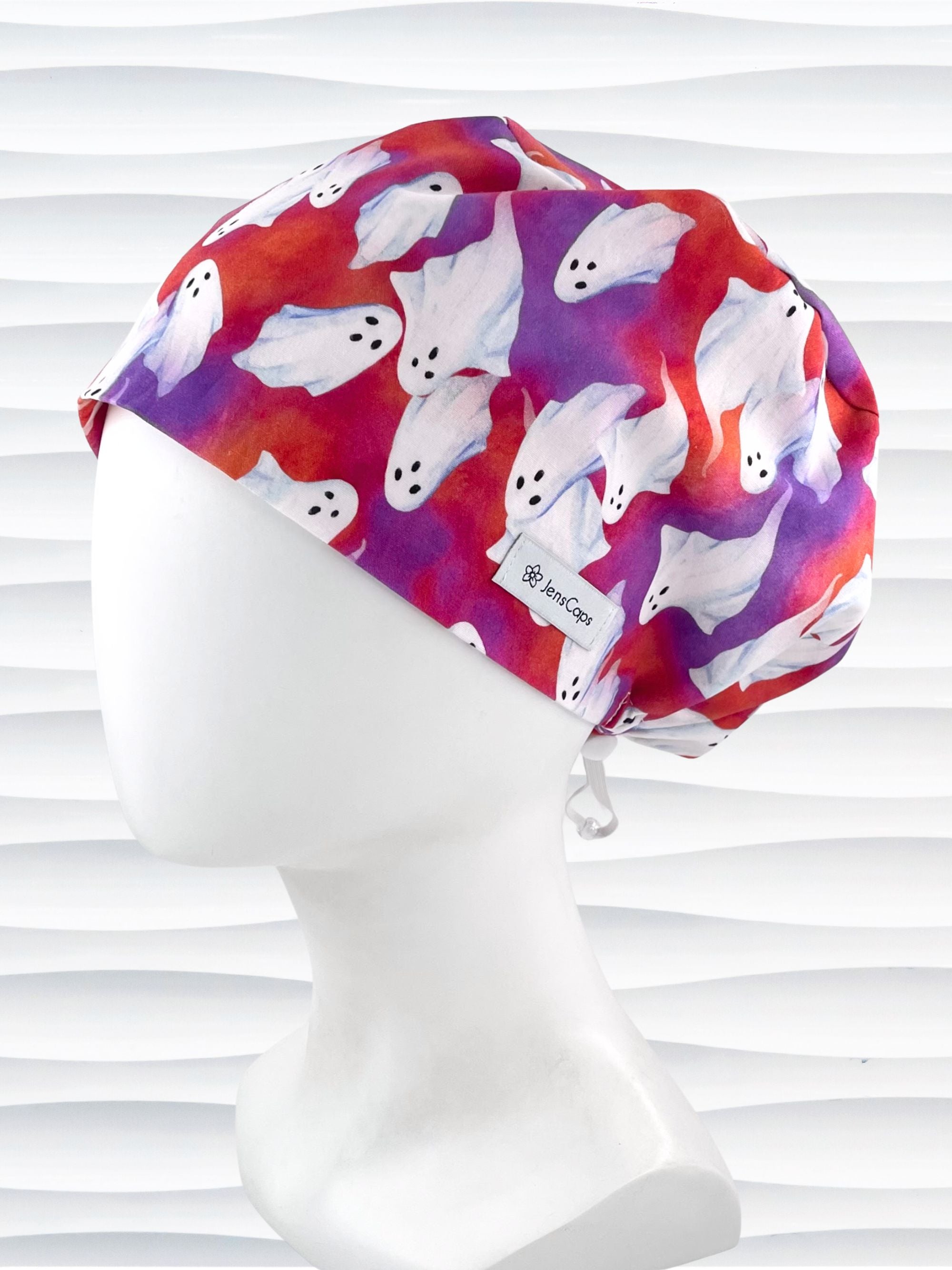 Euro Pixie style surgical scrub cap by JensCaps with white sheet ghosts tossed all aver an ombre red and purple cotton fabric.