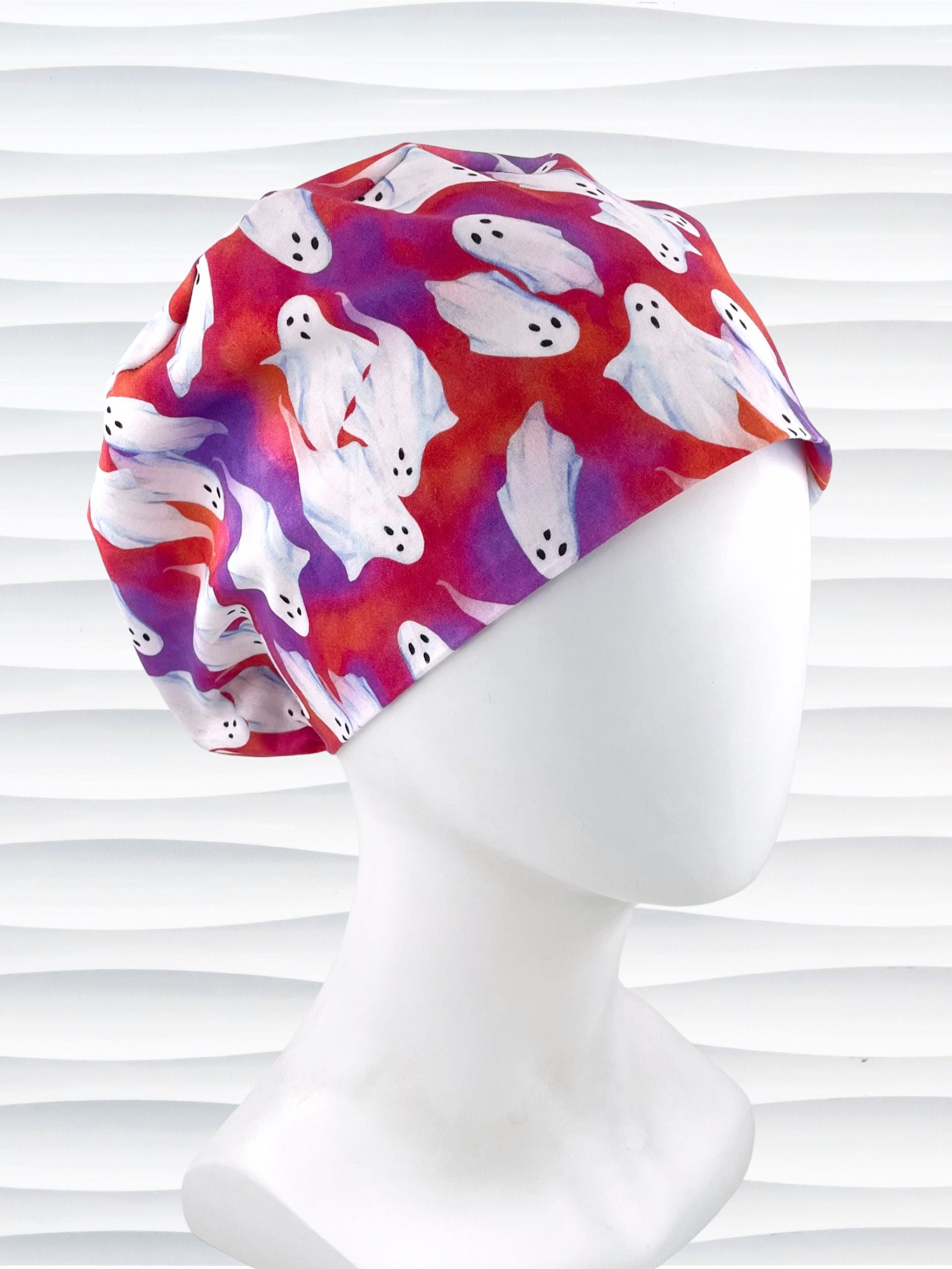 Euro Pixie style surgical scrub cap by JensCaps with white sheet ghosts tossed all aver an ombre red and purple cotton fabric.