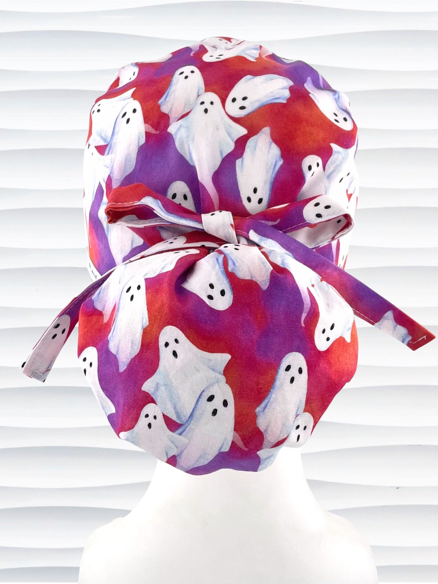 Euro Pony ponytail style surgical scrub cap by JensCaps with white sheet ghosts tossed all aver an ombre red and purple cotton fabric.